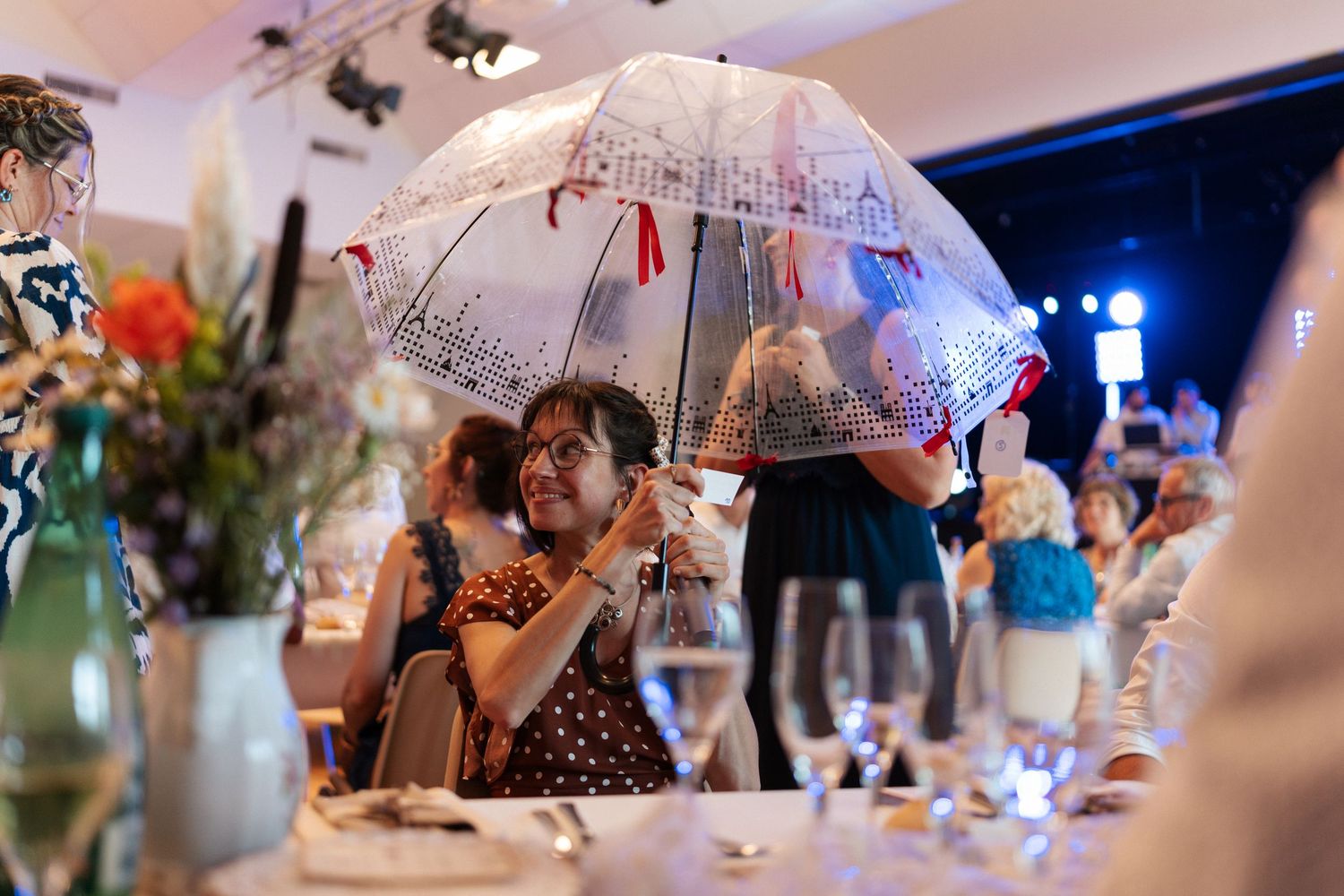 Woman holding a decorative clear umbrella at an elegant wedding reception dinner with floral centerpieces.