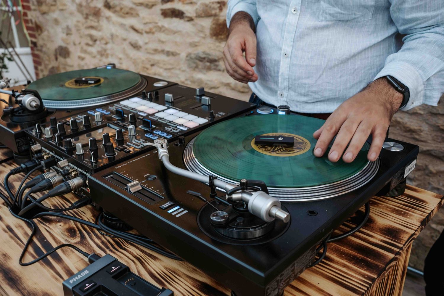 Un DJ mixe de la musique sur des platines vintage dans un lieu de réception de mariage rustique avec un mur en pierre.