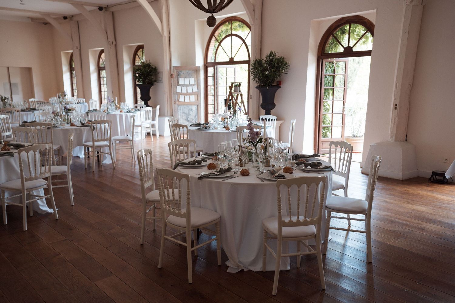 Salle de réception de l’Orangerie des Briottières aux Hauts-d’Anjou – Tables rondes dressées avec lumière naturelle entrant par les baies vi