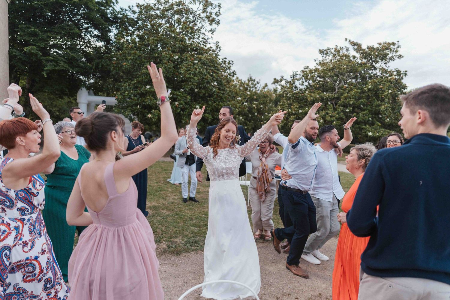 La mariée en robe blanche danse les bras levés au milieu des invités joyeux lors d'un mariage en plein air.