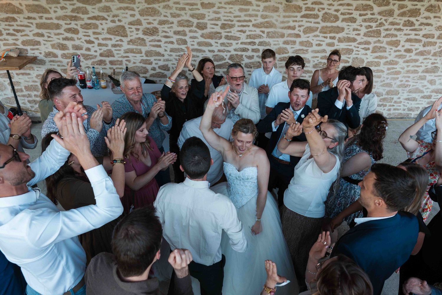 Les invités et les mariés célèbrent joyeusement ensemble sur la piste de danse dans un lieu rustique en pierre.