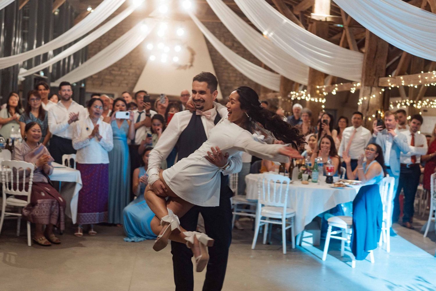 Le marié soulève la mariée lors d'une première danse énergique à la réception de mariage champêtre dans une grange.