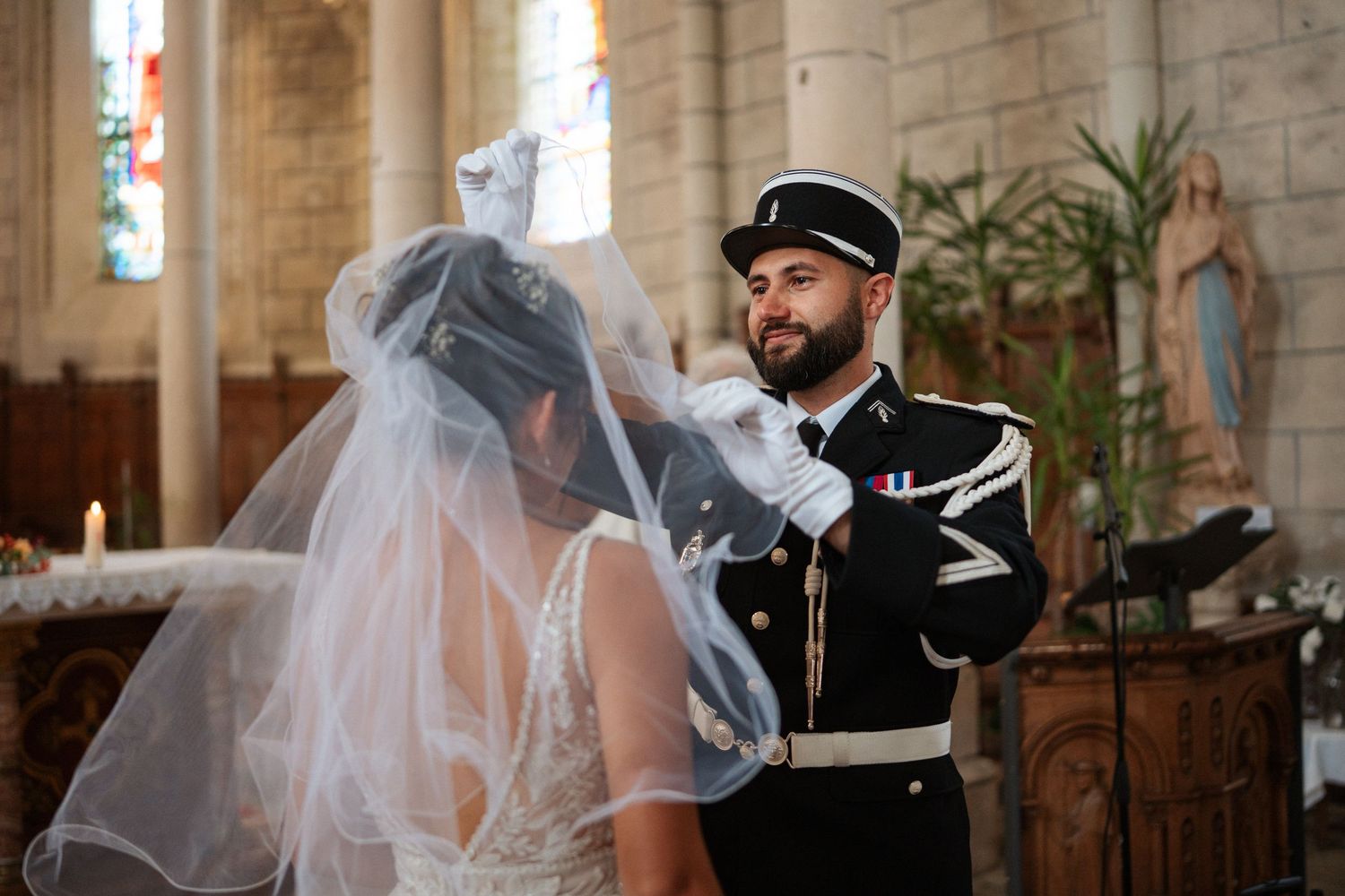 Groom in military uniform lifting bride's veil during wedding ceremony inside a historic church.