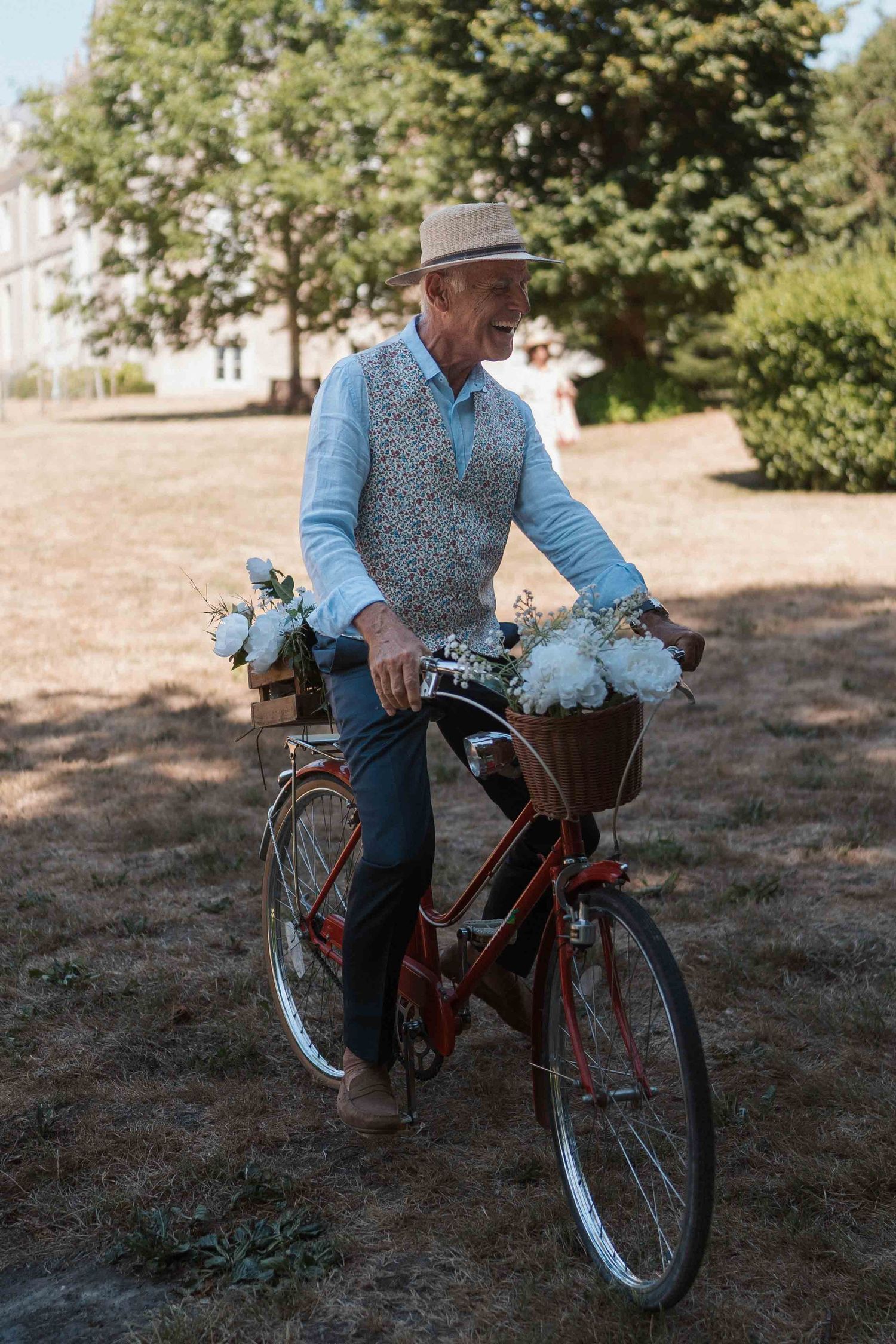 Un homme âgé circule à vélo dans un parc ensoleillé, sur un modèle vintage rouge orné de fleurs blanches.