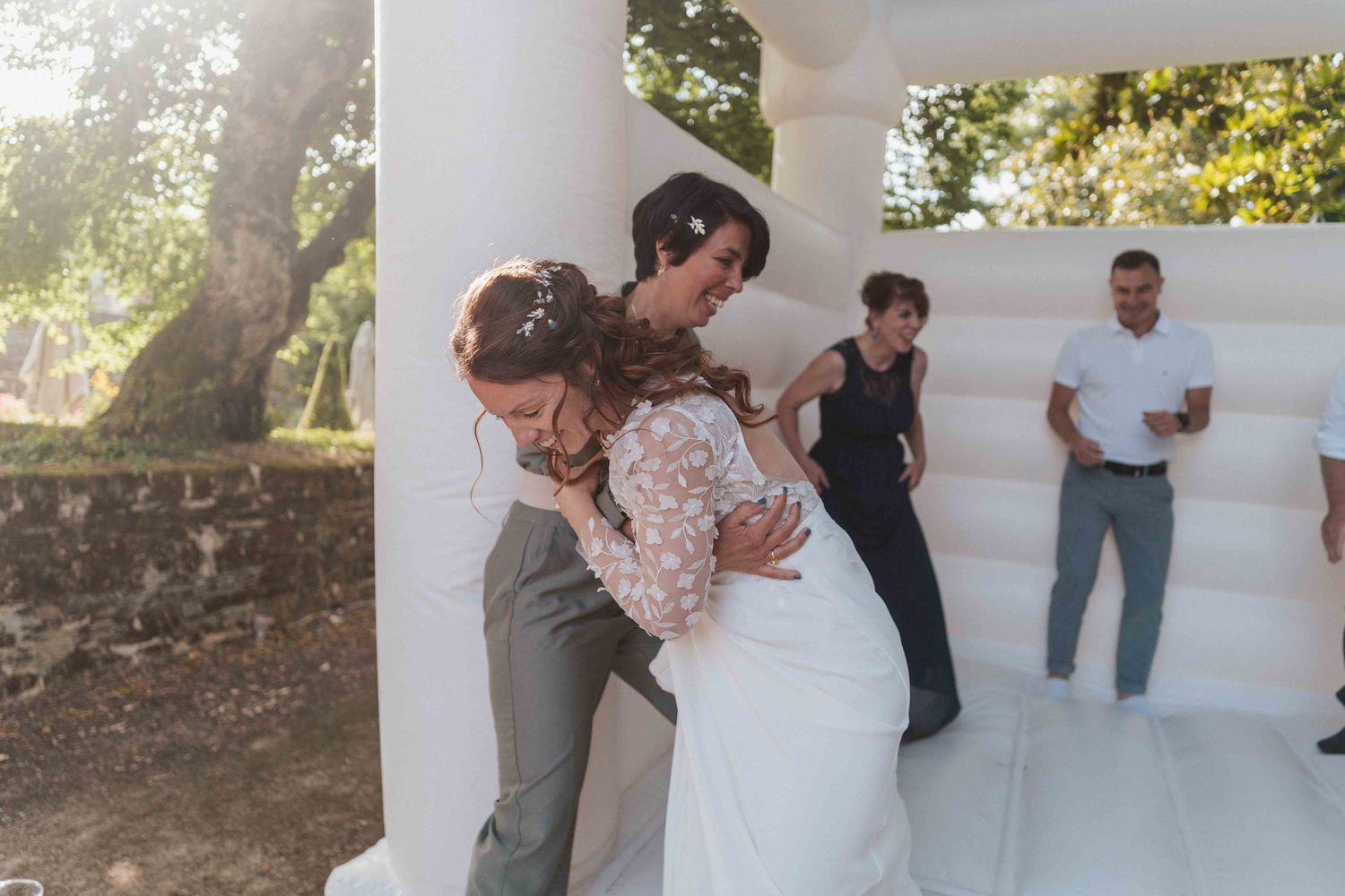 La mariée en robe de dentelle embrasse un invité près d'un château gonflable blanc lors d'une réception de mariage en plein air.