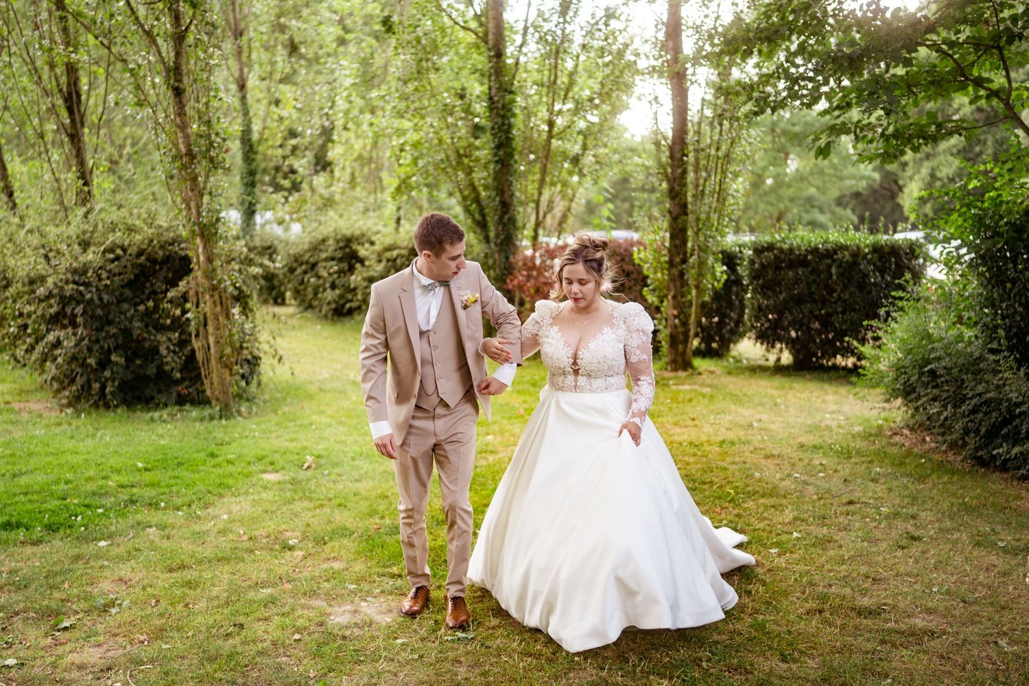 Couple de mariés se promenant main dans la main dans le jardin verdoyant de l’Orangerie de Maulny à Angers.