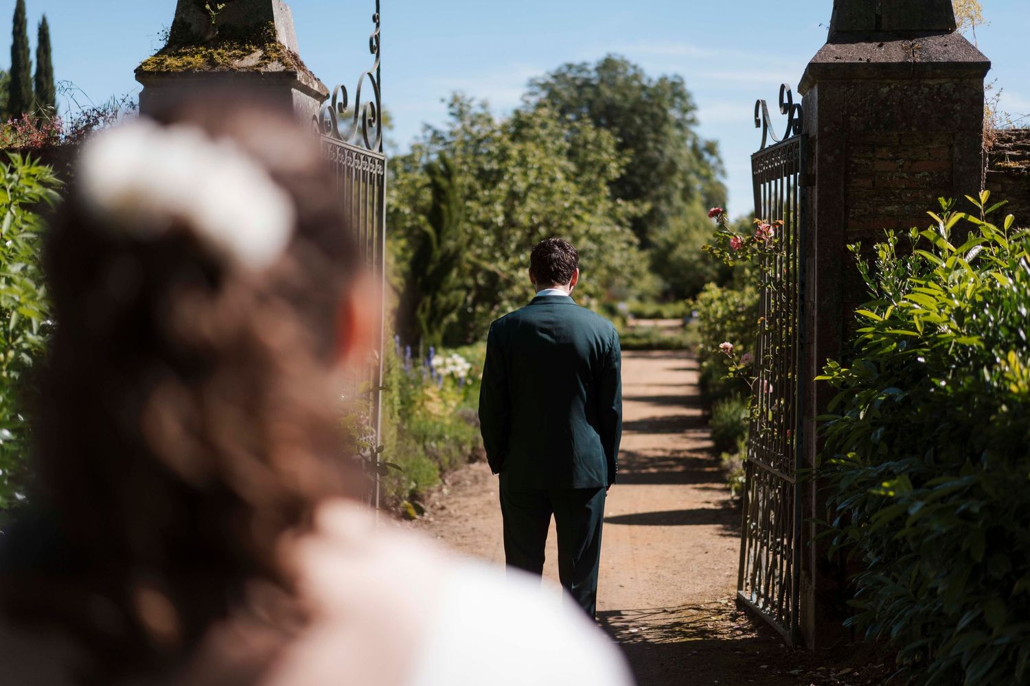 Les mariés franchissent d'élégantes portes de jardin le jour de leur mariage, entourés d'une végétation luxuriante.