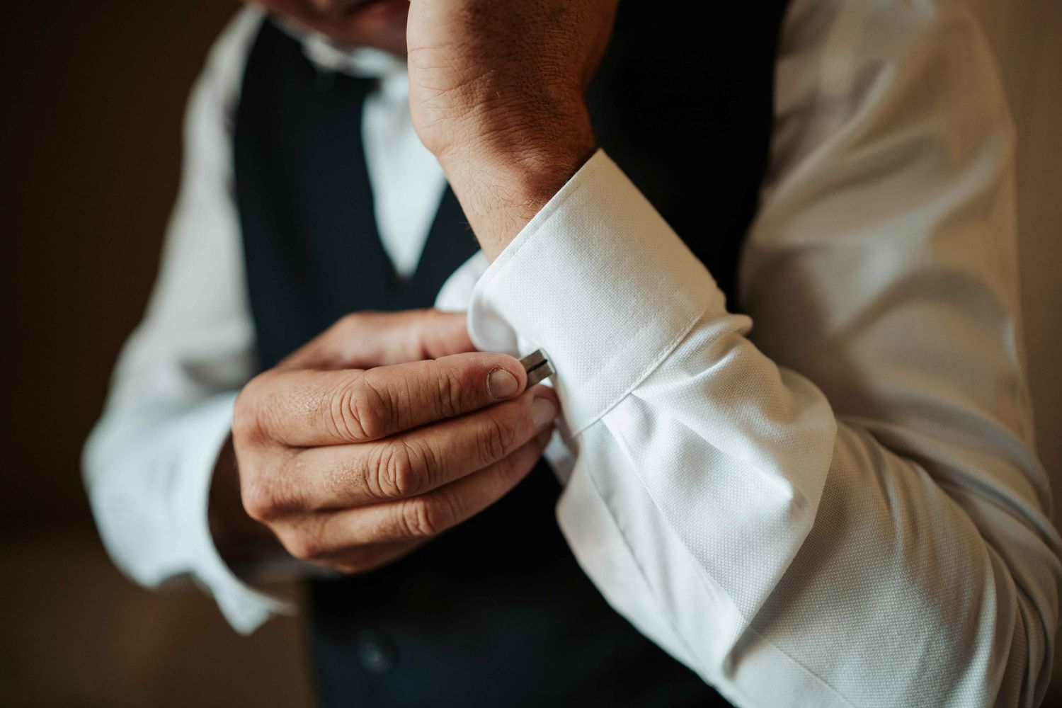 Le marié ajuste ses boutons de manchette en argent aux manches de sa chemise blanche avant la cérémonie de mariage.