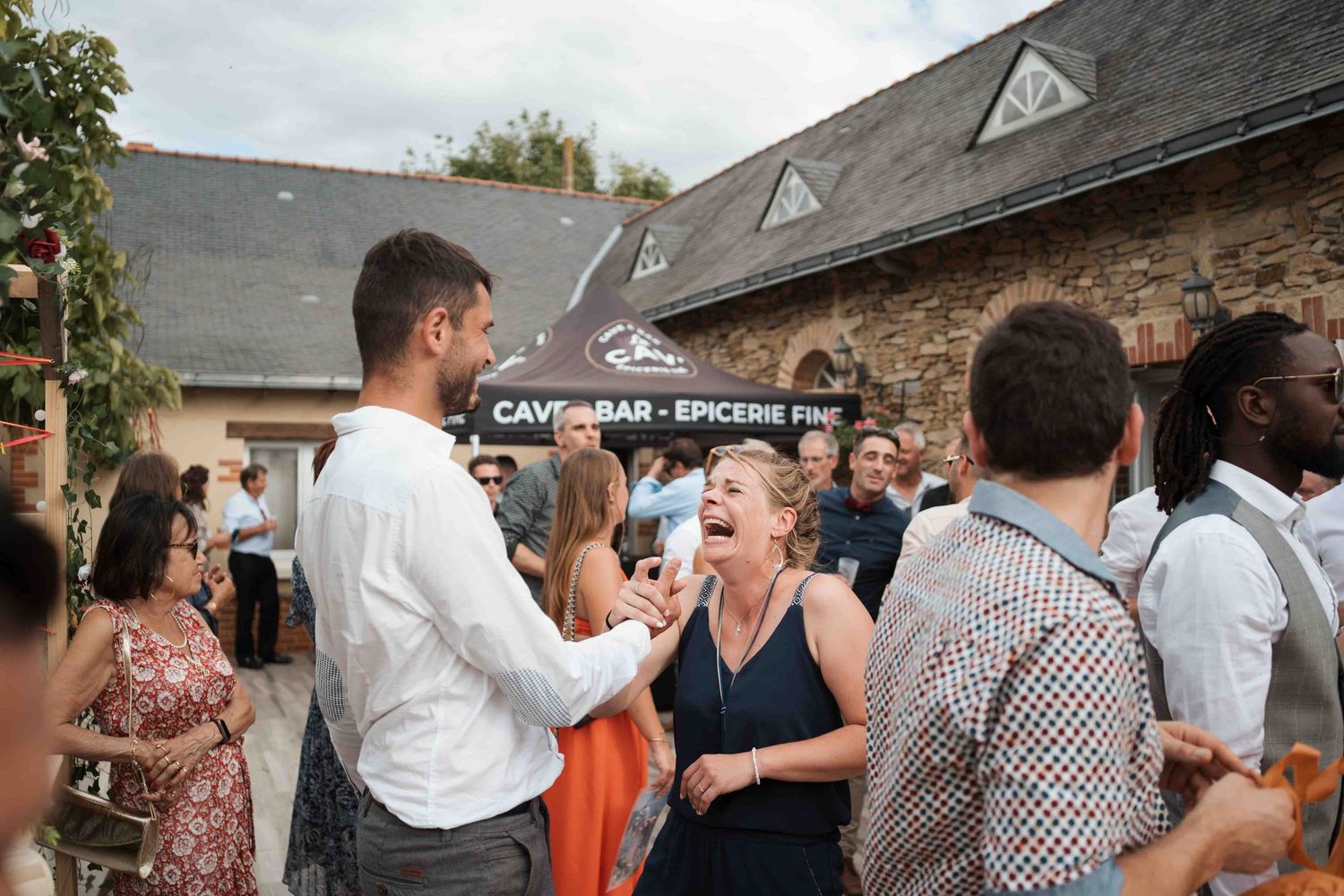 Les invités du mariage rient et discutent à l'extérieur d'un bar rustique troglodyte et d'une épicerie fine.