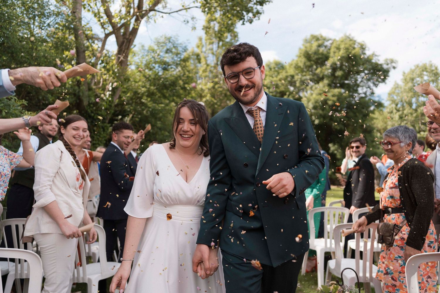 Sortie de cérémonie avec lancer de pétales – Mariés souriants sous une pluie de fleurs, entourés de leurs invités dans un cadre champêtre.