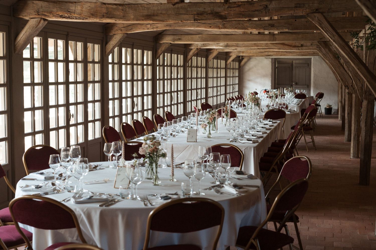 Salle de réception au Château de la Perrière à Avrillé – Grandes tables élégamment dressées dans une salle lumineuse aux poutres apparentes.
