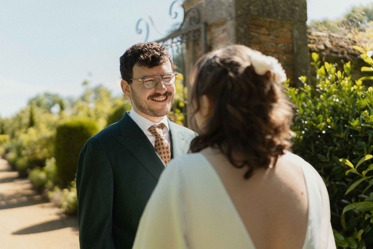 Un marié souriant en costume vert partage un moment de premier regard avec sa mariée en extérieur.