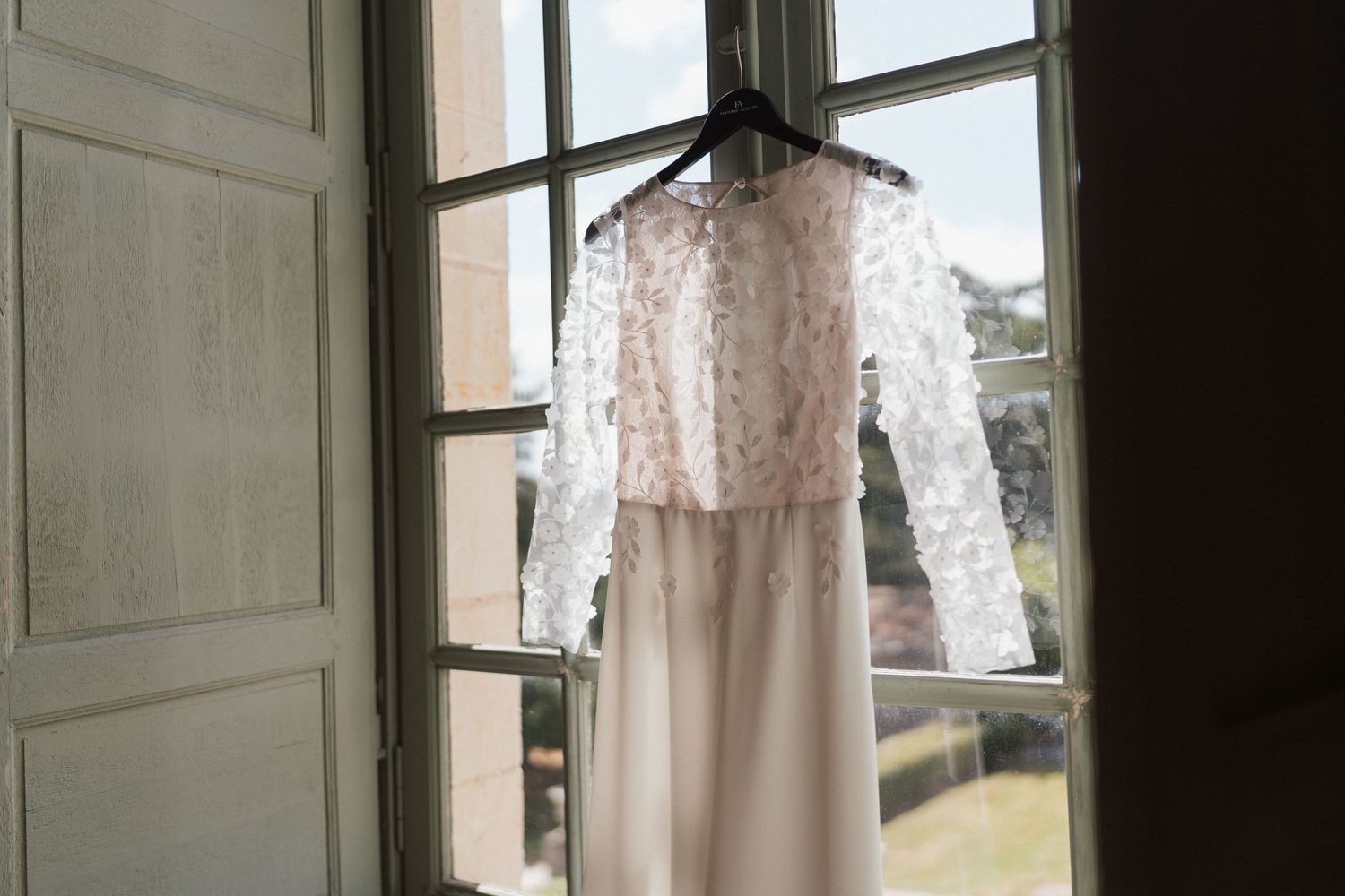 Robe de mariée suspendue à une fenêtre du Château de la Perrière à Avrillé – Préparatifs dans un cadre élégant et lumineux.