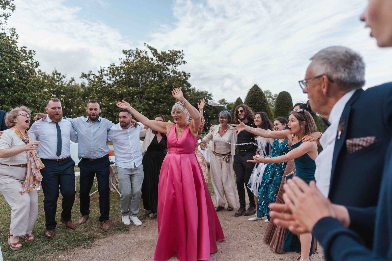 Des invités de mariage dansent à l'extérieur, une femme en robe rose levant les bras pendant les festivités.