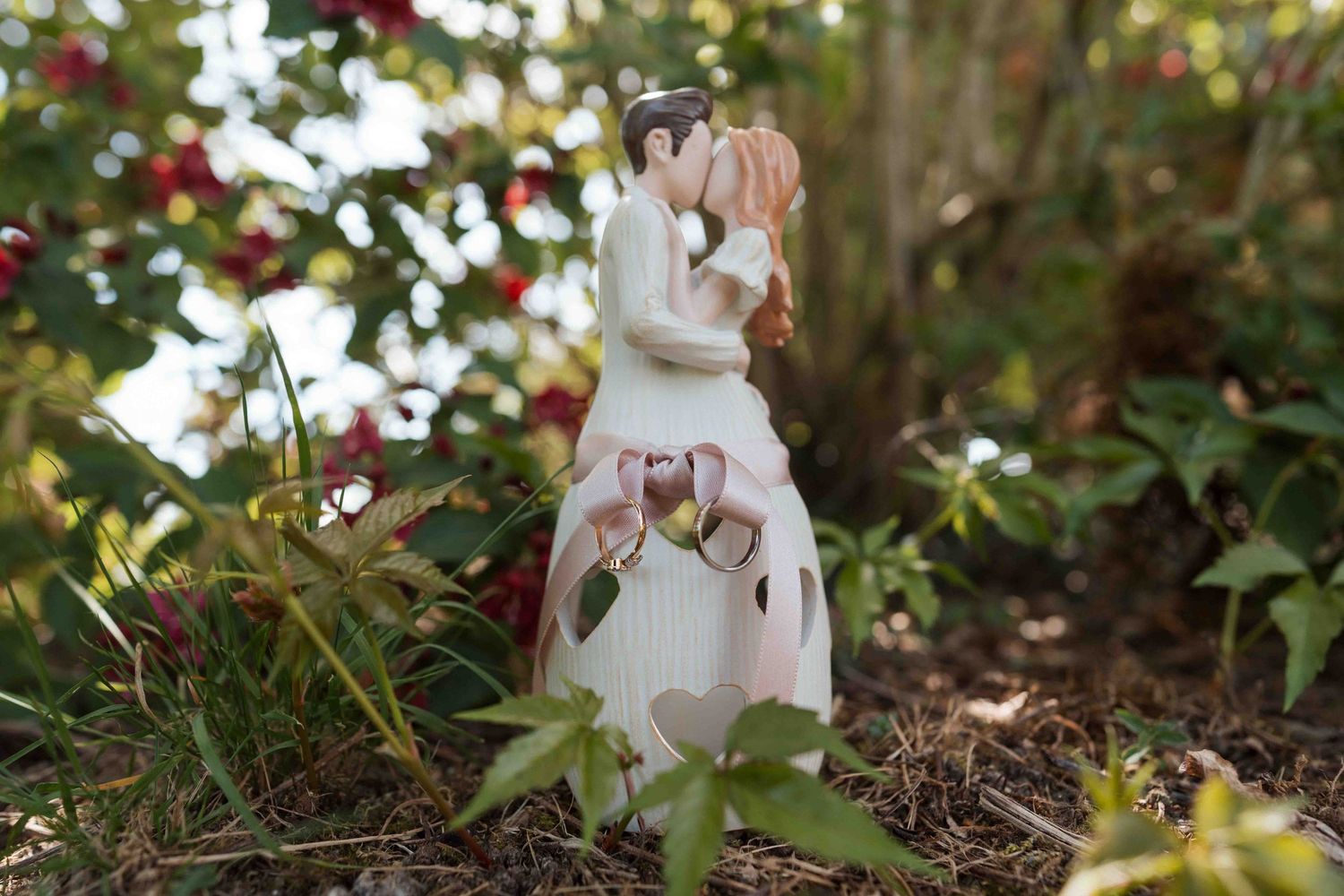Figurine en céramique pour gâteau de mariage représentant les mariés s'embrassant, exposée à l'extérieur parmi un feuillage vert luxuriant