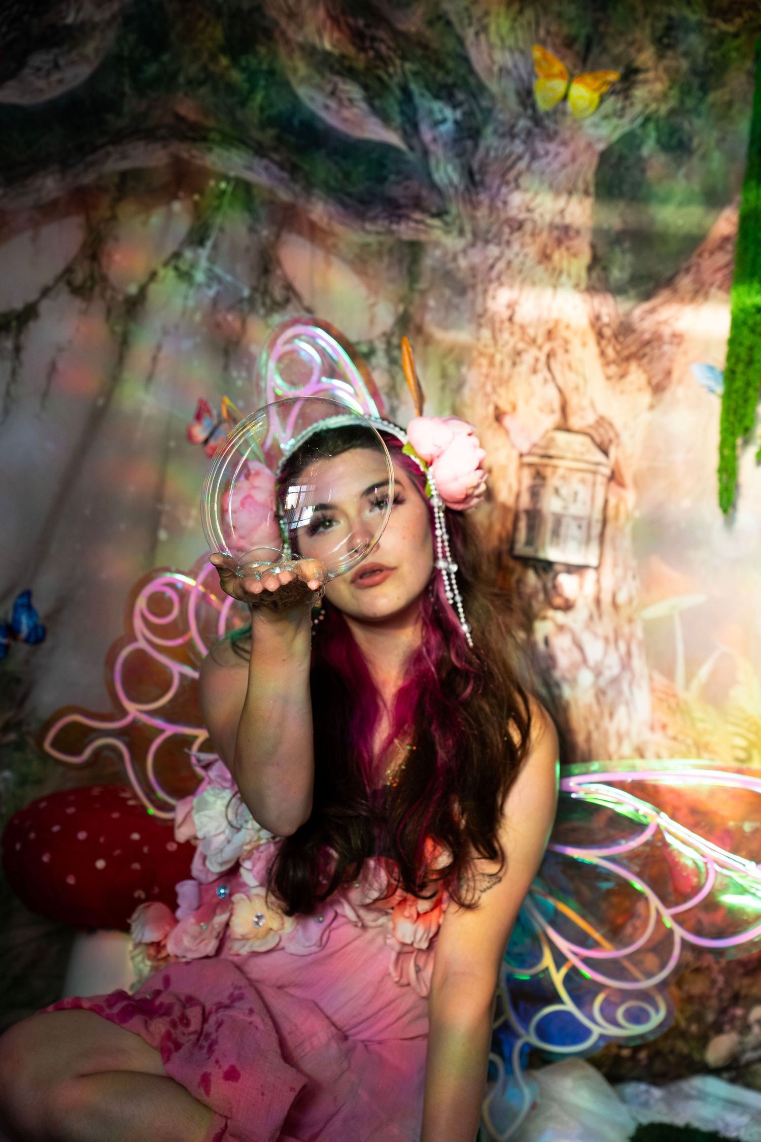 Young woman in pink fairy costume holding a glass sphere in an enchanted forest set. Fantasy Photoshoot