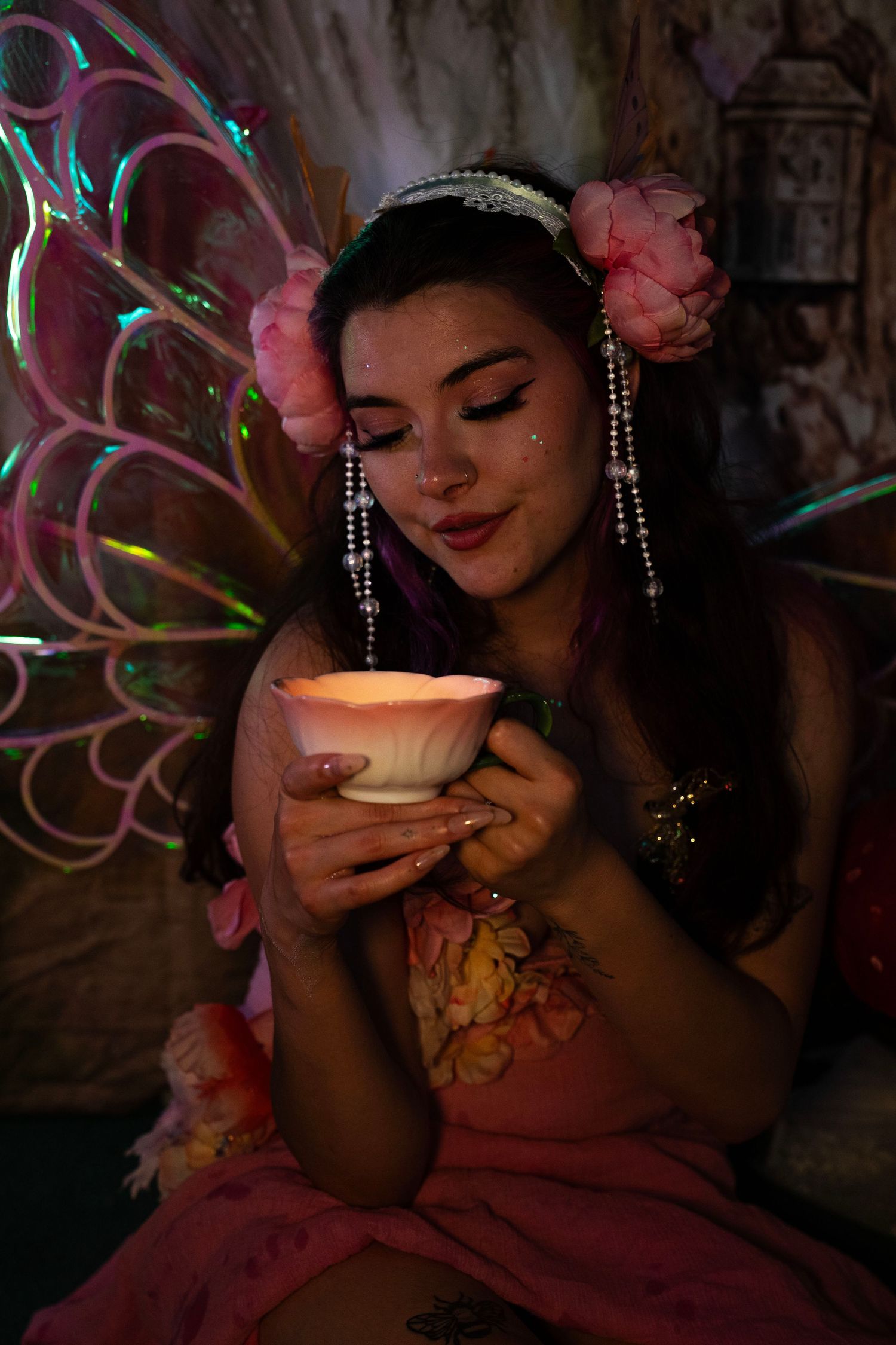 A fairy cosplay model in pink floral dress holds a glowing lotus cup in a magical dark setting. Fantasy Photoshoot