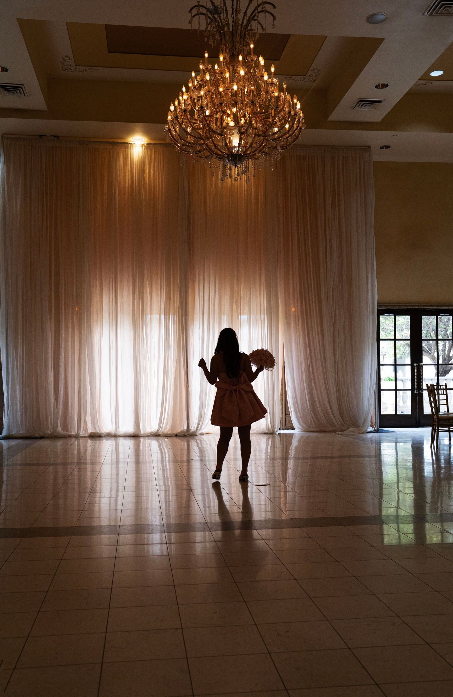Silhouette of woman in pink dress under chandelier in elegant ballroom.