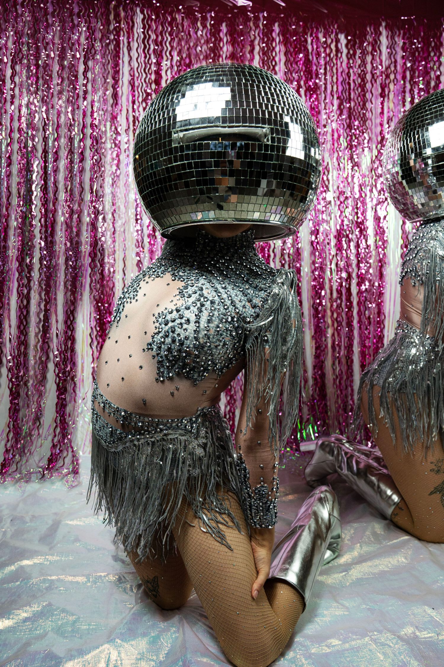 Close-up of performer in silver rhinestone fringe costume wearing large mirrored disco ball helmet.
