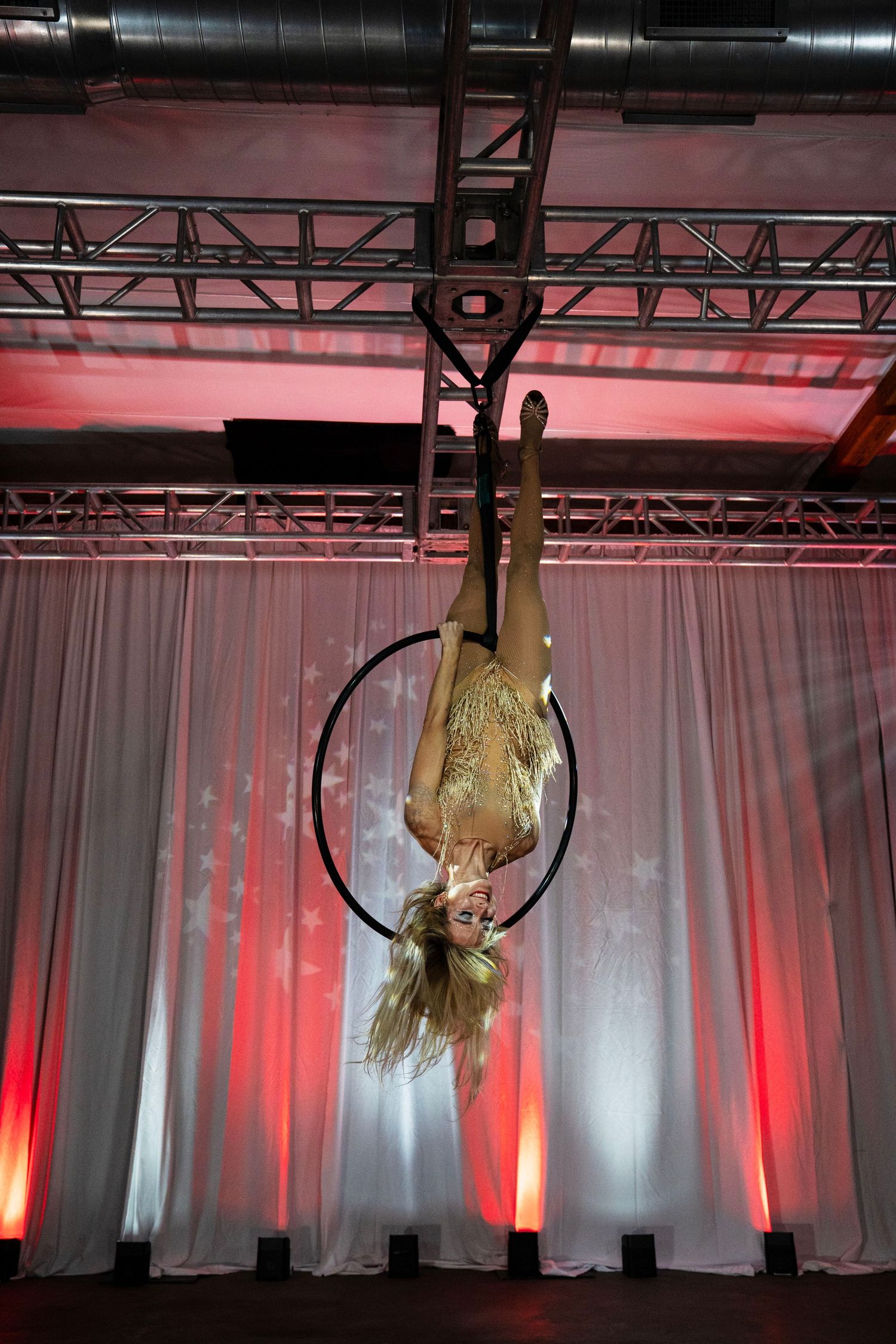 Aerialist in gold costume performs inverted aerial hoop routine suspended from stage rigging. Circus Photoshoot