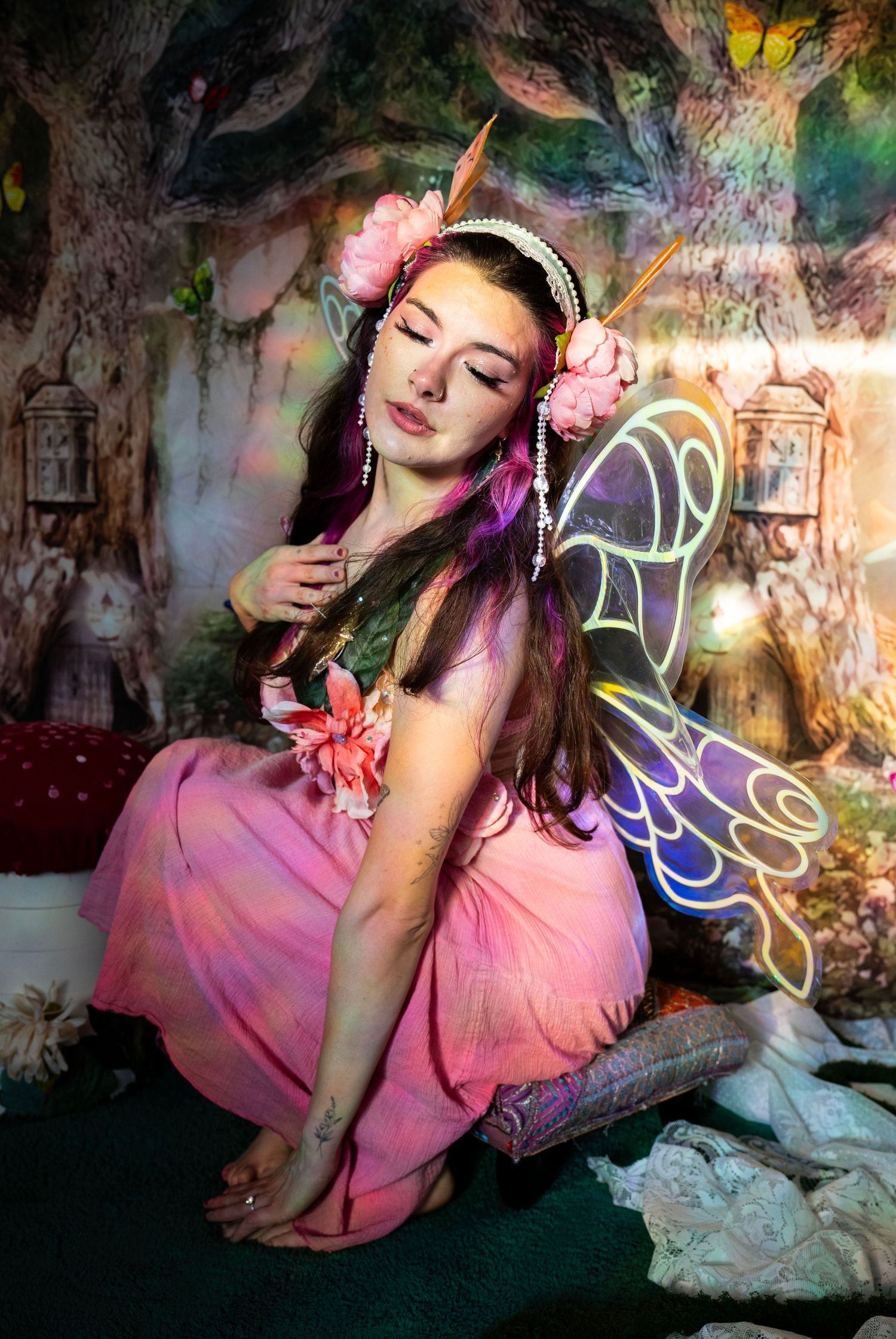 Woman in pink fairy costume with colorful butterfly wings and floral crown, eyes closed in enchanted forest. Fantasy Photoshoot