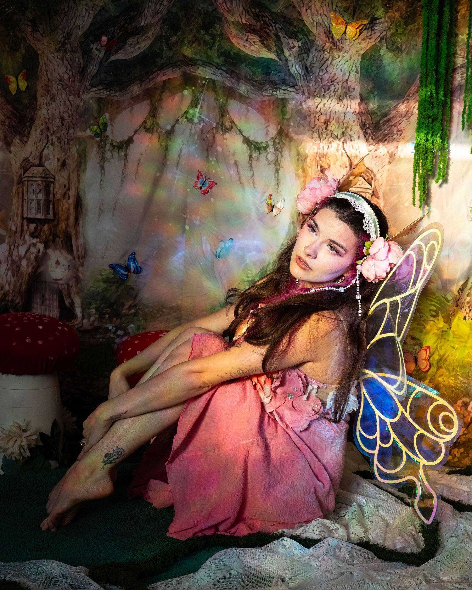 Woman in fairy costume with butterfly wings sitting in a magical woodland photography set. Fantasy Photoshoot