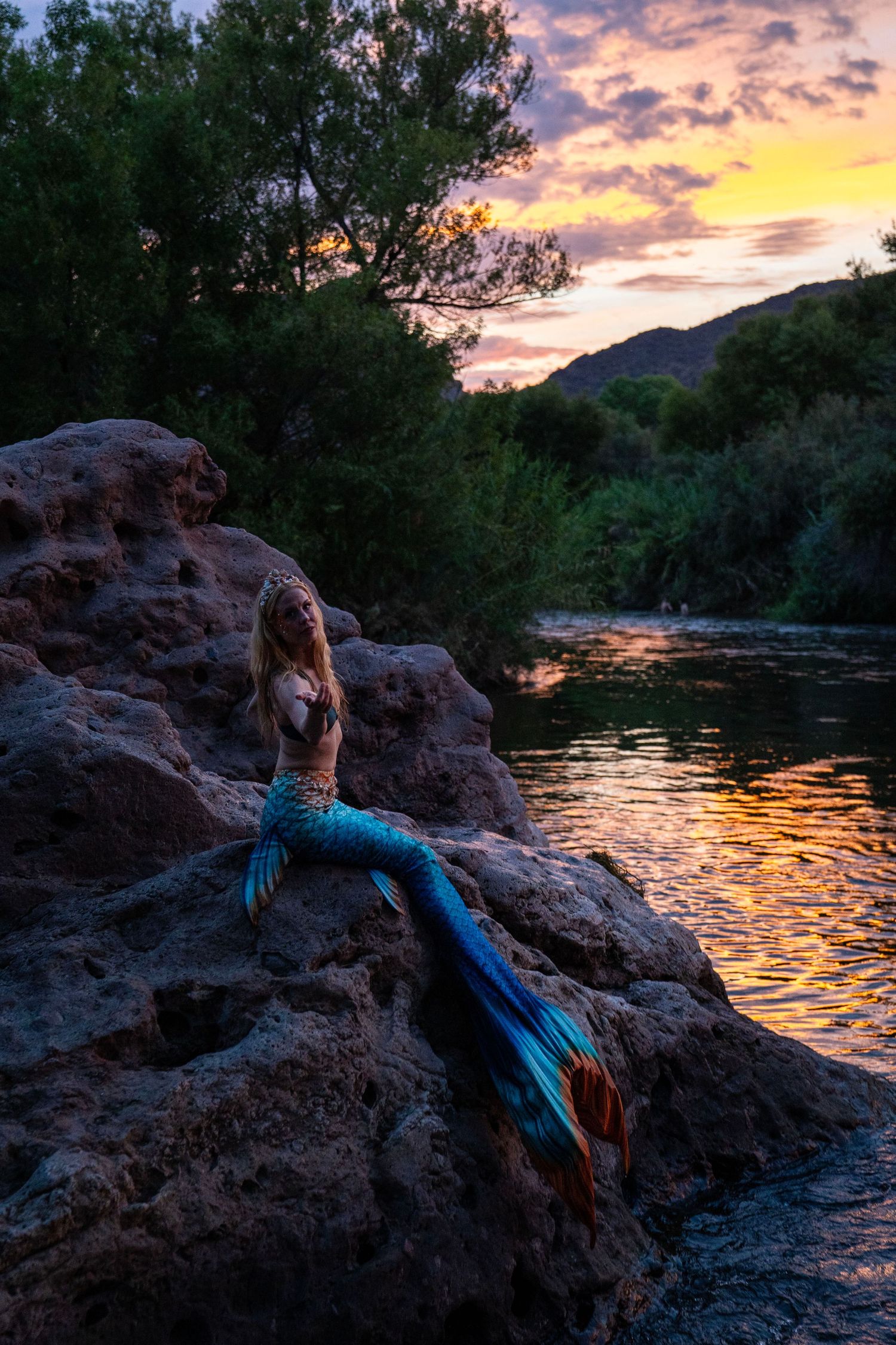 Woman in colorful mermaid costume posing on rocks by a river at sunset. Mermaid photoshoot, fantasy photoshoot. Arizona photographer.