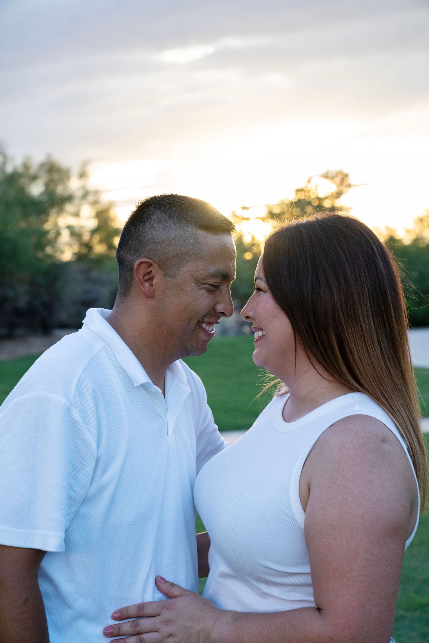 Happy couple in matching white tops smile at each other during a romantic golden hour outdoor photo session.