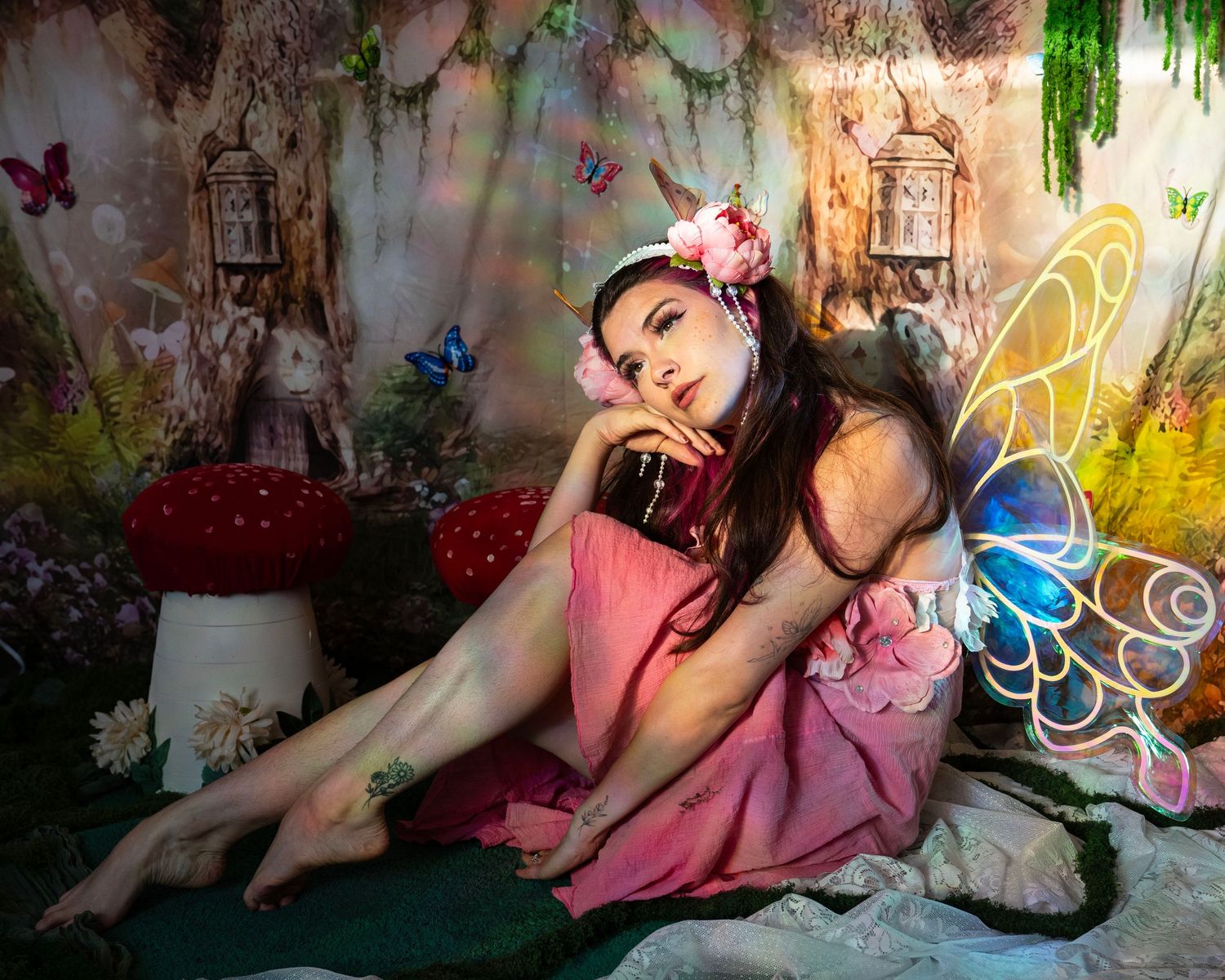 Young woman in pink fairy dress resting near a giant mushroom in an enchanted forest set. Fantasy Photoshoot