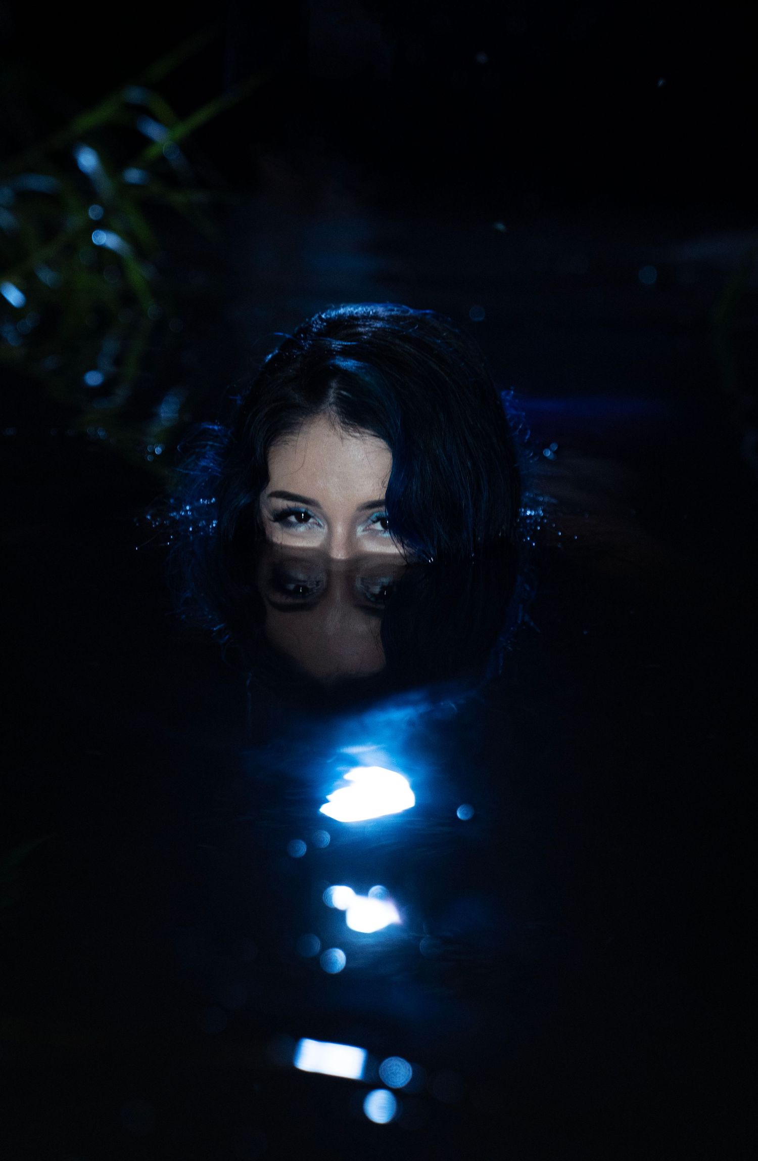 Mysterious woman submerged in dark water with only eyes visible above surface at night.