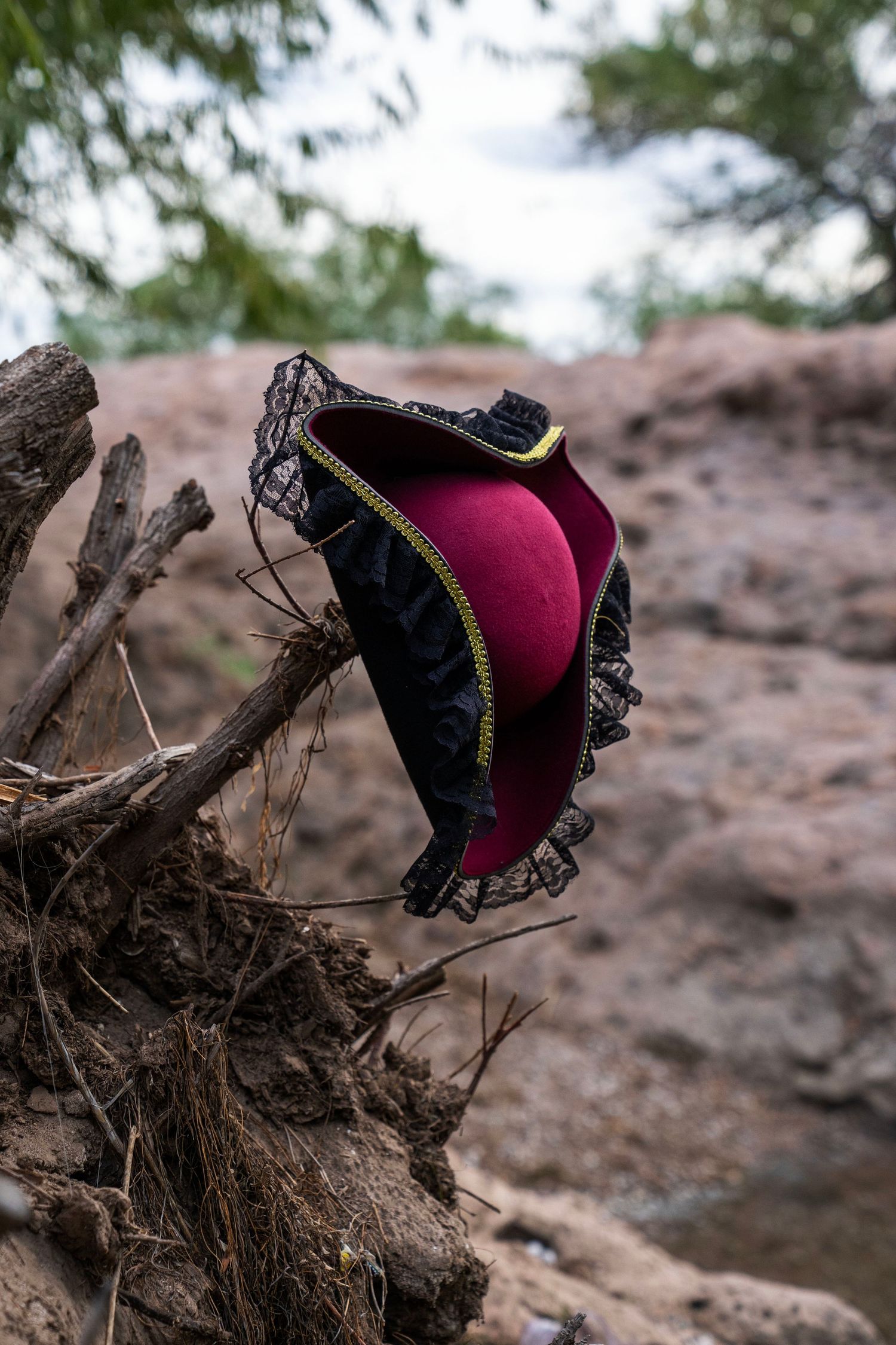 A decorative red and black pirate hat with gold trim rests on driftwood outdoors. Fantasy Photoshoot