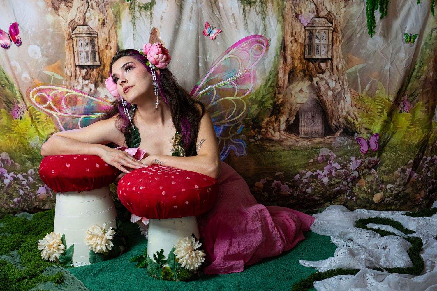 Woman dressed as fairy sits on mushroom props in enchanted forest photo set. Fantasy Photoshoot