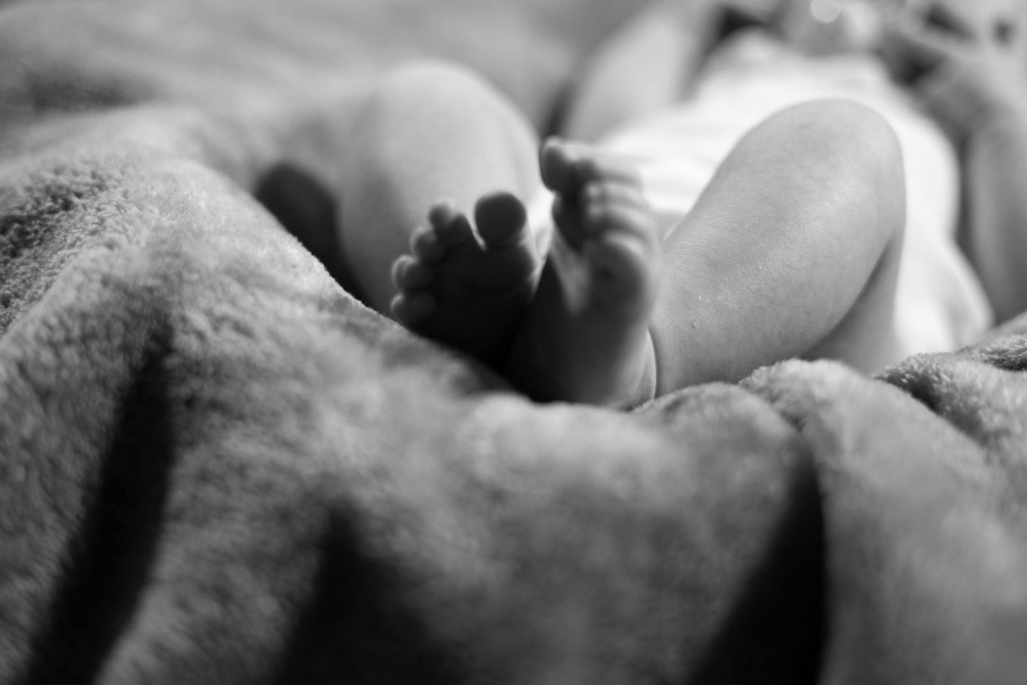 Black and white close-up photo of newborn baby feet resting on a soft fluffy blanket.