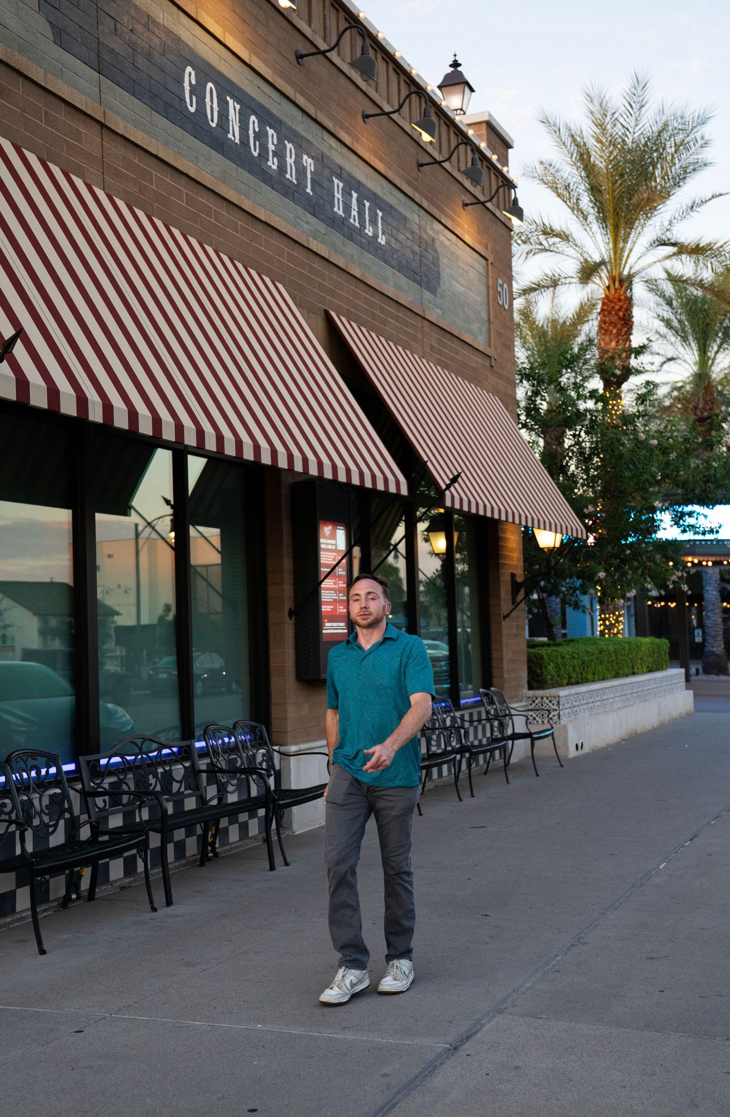 Man standing in front of a Concert Hall with red and white striped awnings on a sunny day.