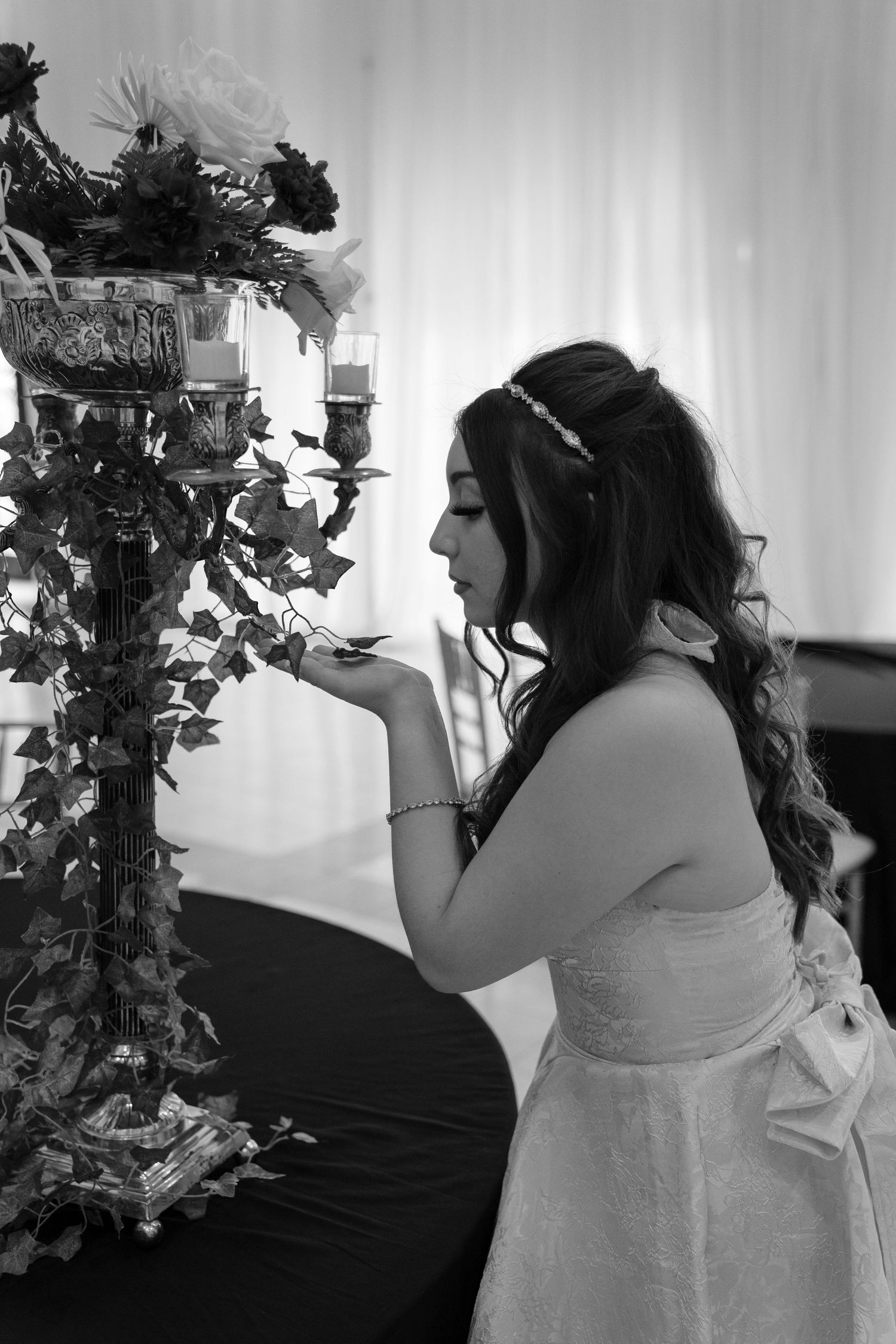 Black and white photo of a bride in a strapless gown lighting a candle on an ornate floral candelabra.
