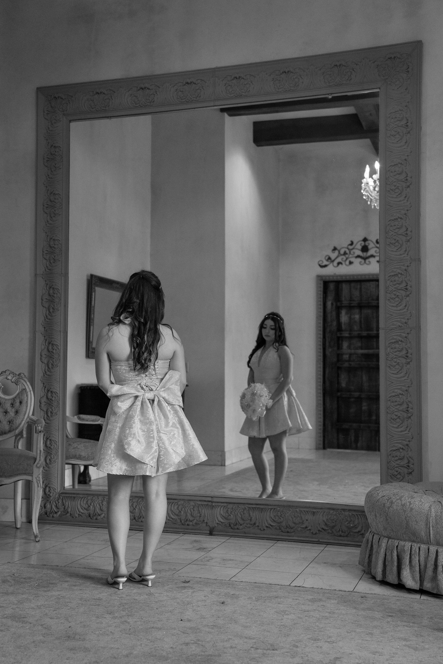 Black and white photo of woman in pink dress reflected in ornate mirror.