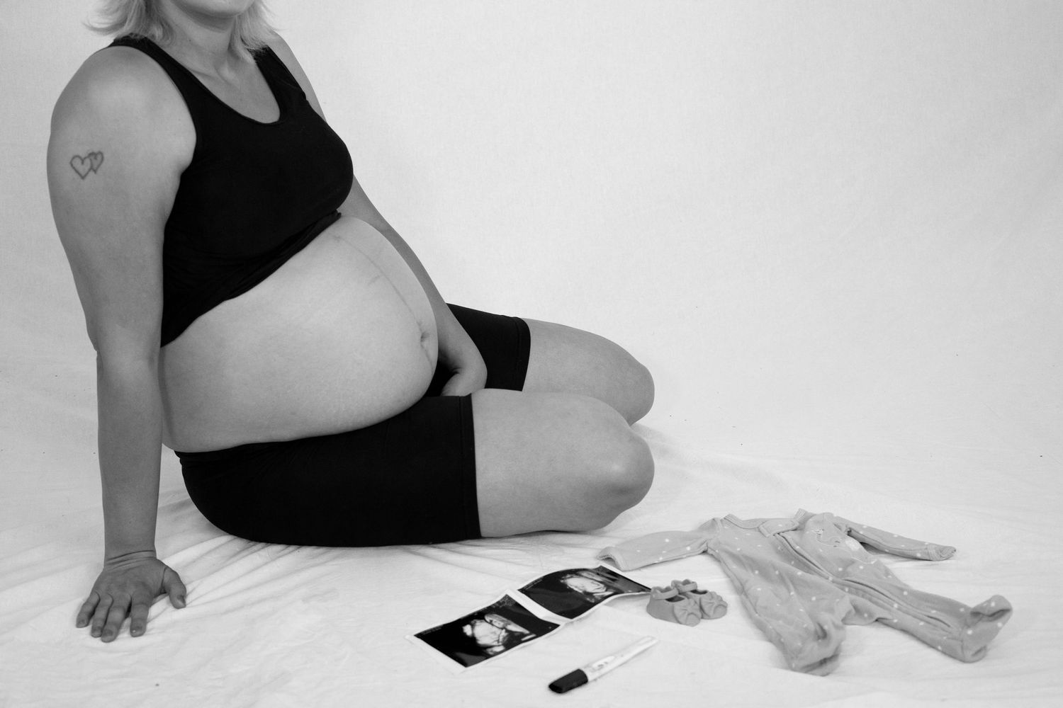 Black and white photo of pregnant woman sitting with ultrasound photos and baby gloves nearby.