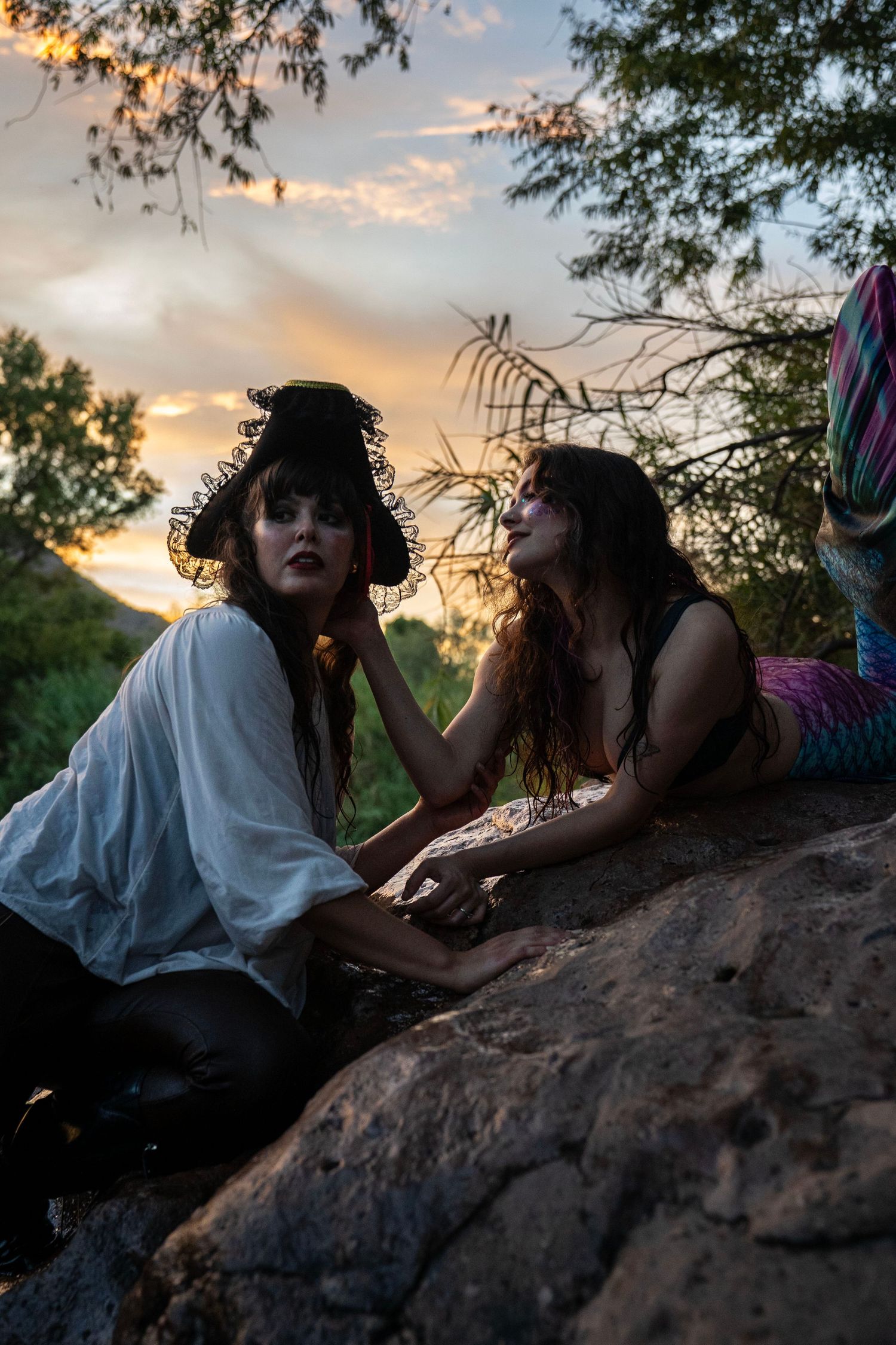 Two women in pirate and mermaid costumes posing dramatically on rocks at dusk. Mermaid photoshoot, fantasy photoshoot. Arizona photographer.