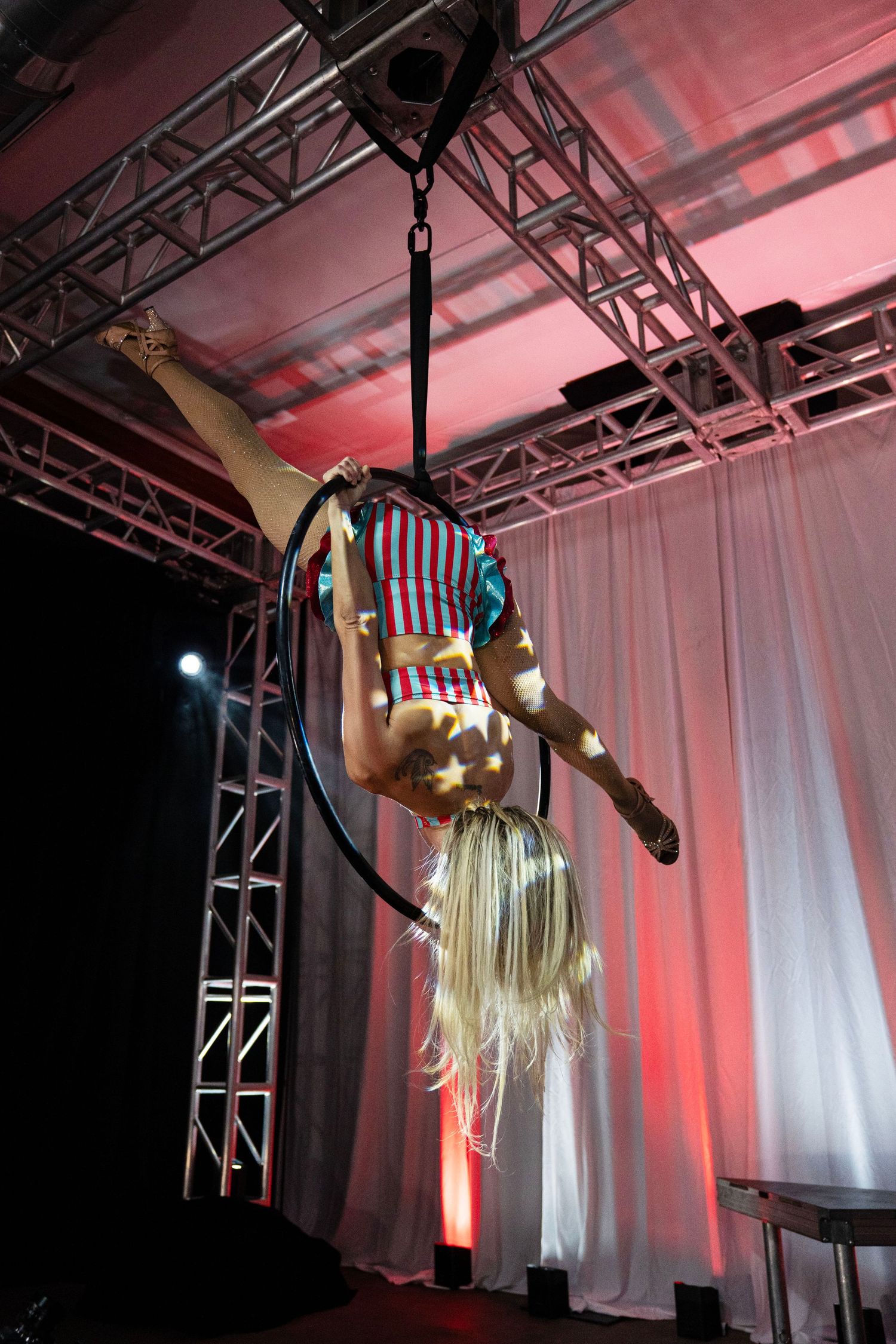 Blonde aerial hoop performer hanging upside down in patriotic costume under stage lighting. Circus Photoshoot