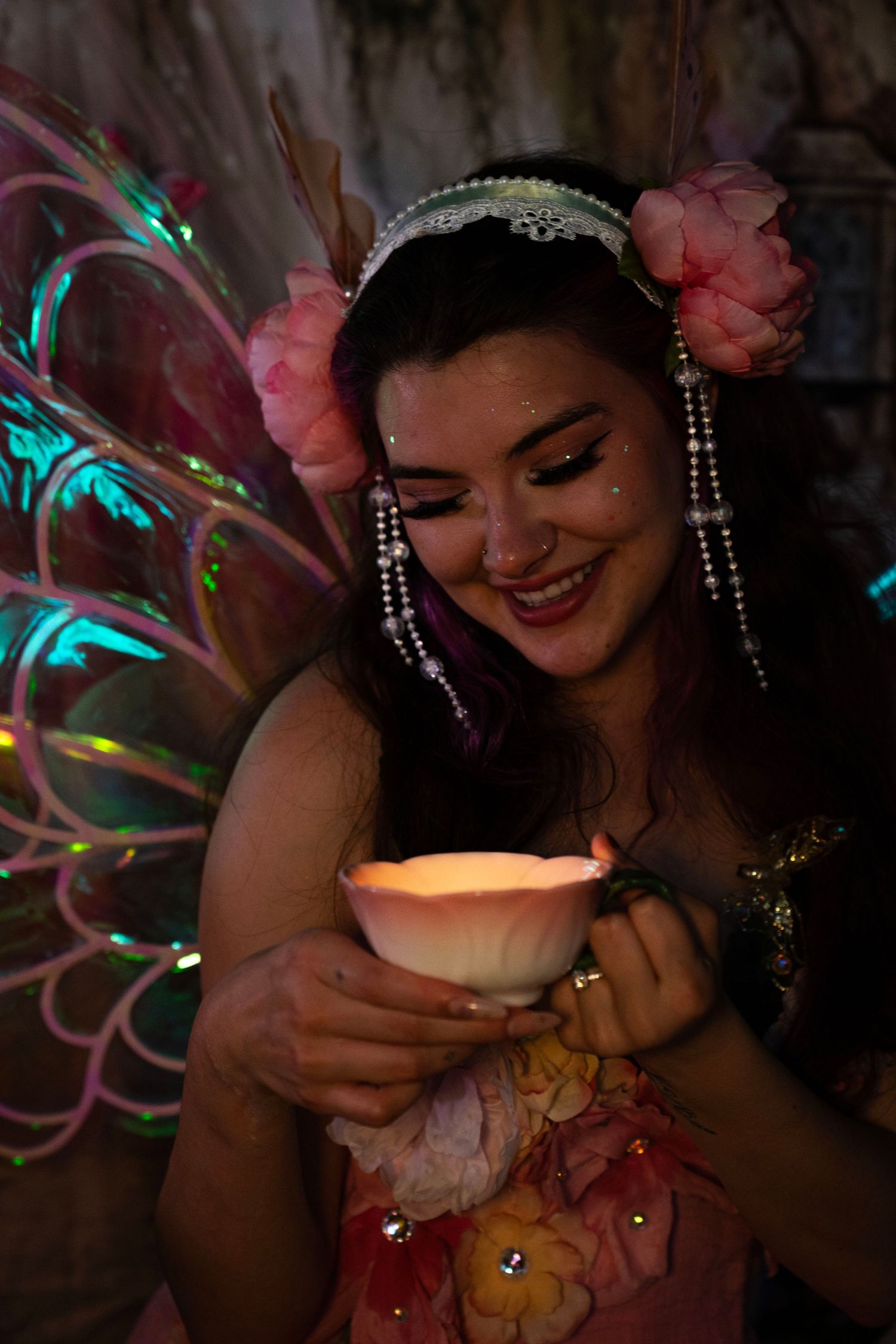 Fairy costume model with pearl headband and glowing lotus candle smiles in magical dark forest setting. Fantasy Photoshoot