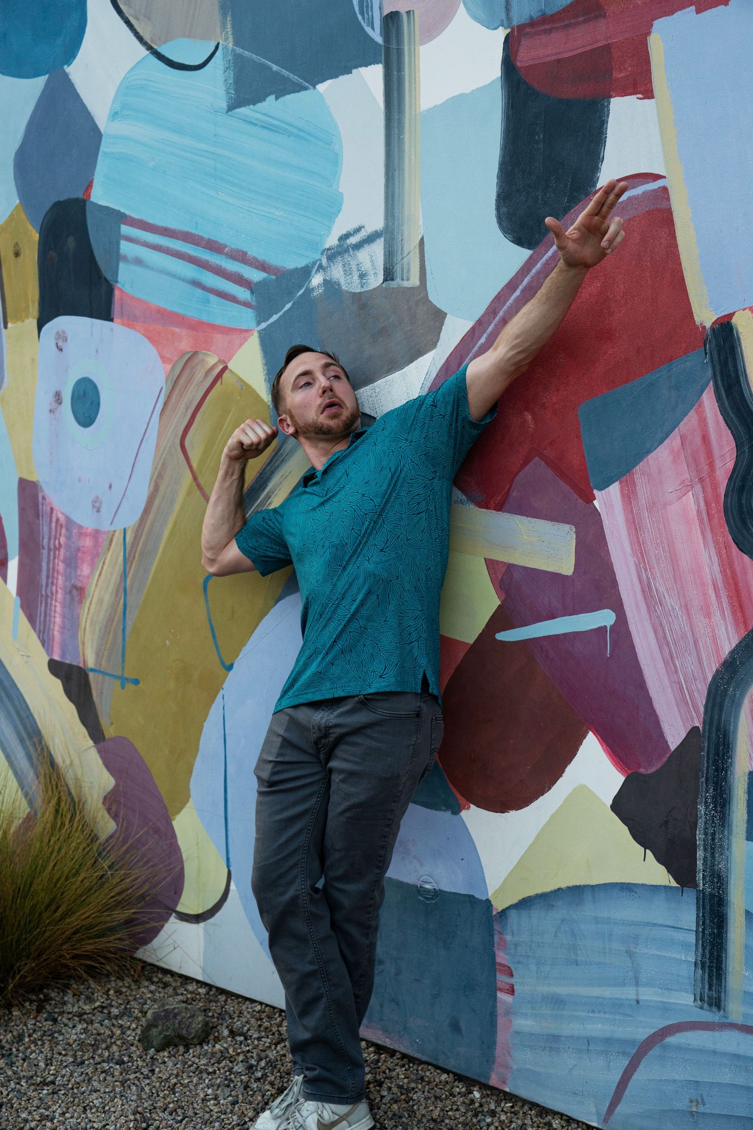 Man in teal shirt posing dynamically against vibrant colorful abstract painted wall.