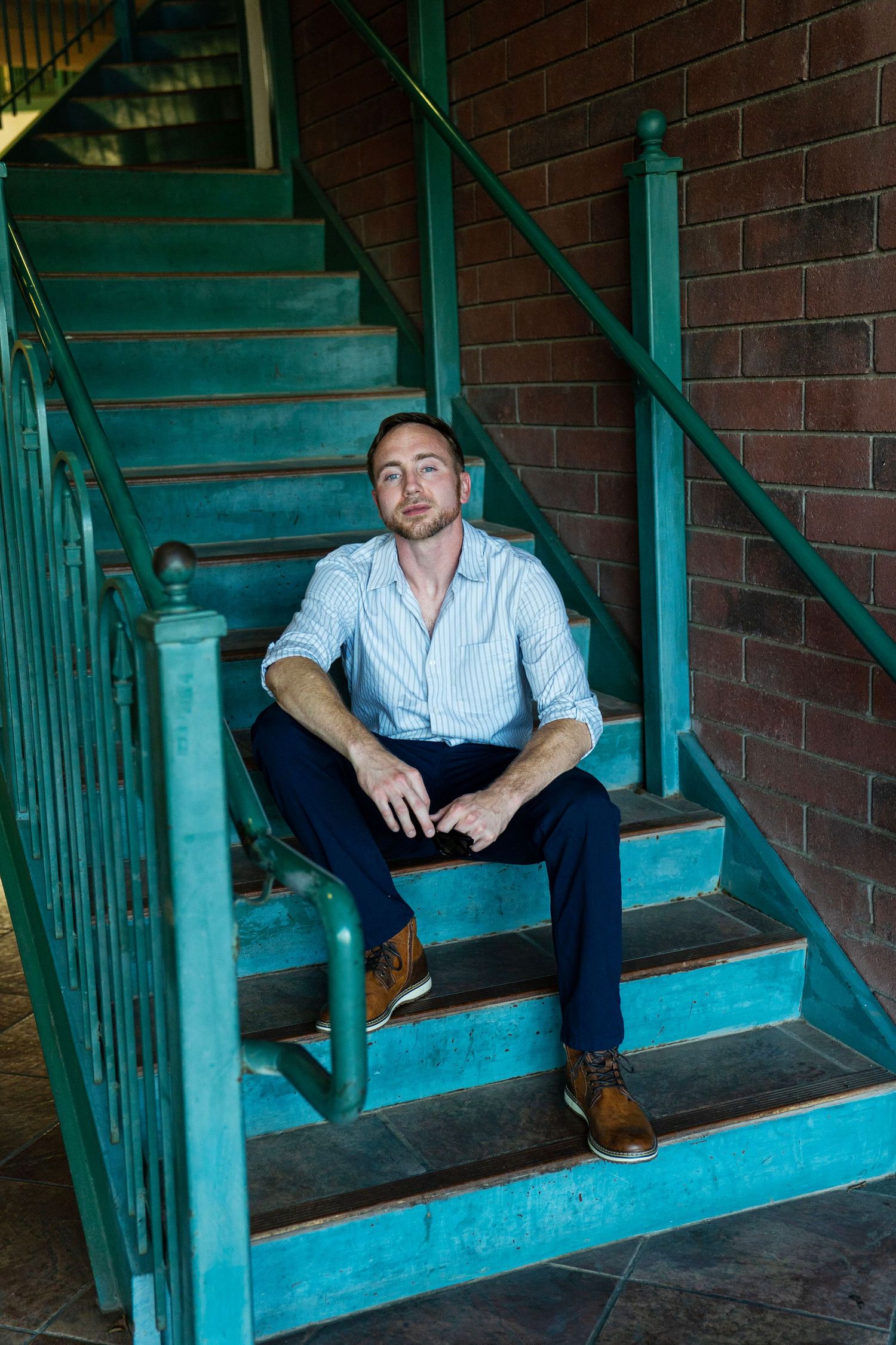 Man in striped shirt and navy pants sits relaxed on teal vintage staircase.