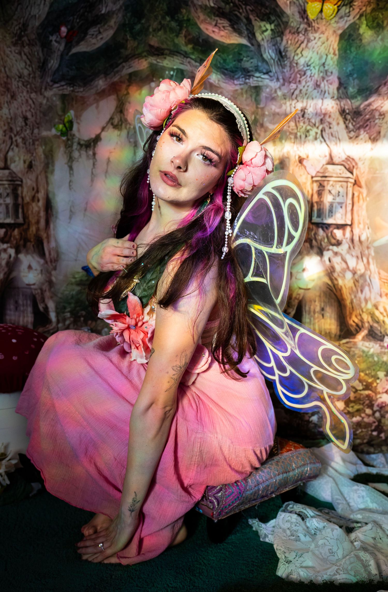 Woman in pink fairy dress with purple-blue wings and pink floral headpiece in magical forest photo studio. Fantasy Photoshoot