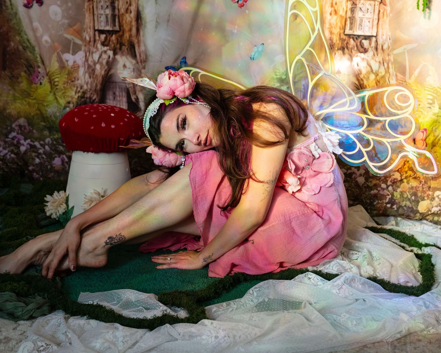 Woman in pink fairy dress with glowing wings resting in an enchanted forest photo studio. Fantasy Photoshoot