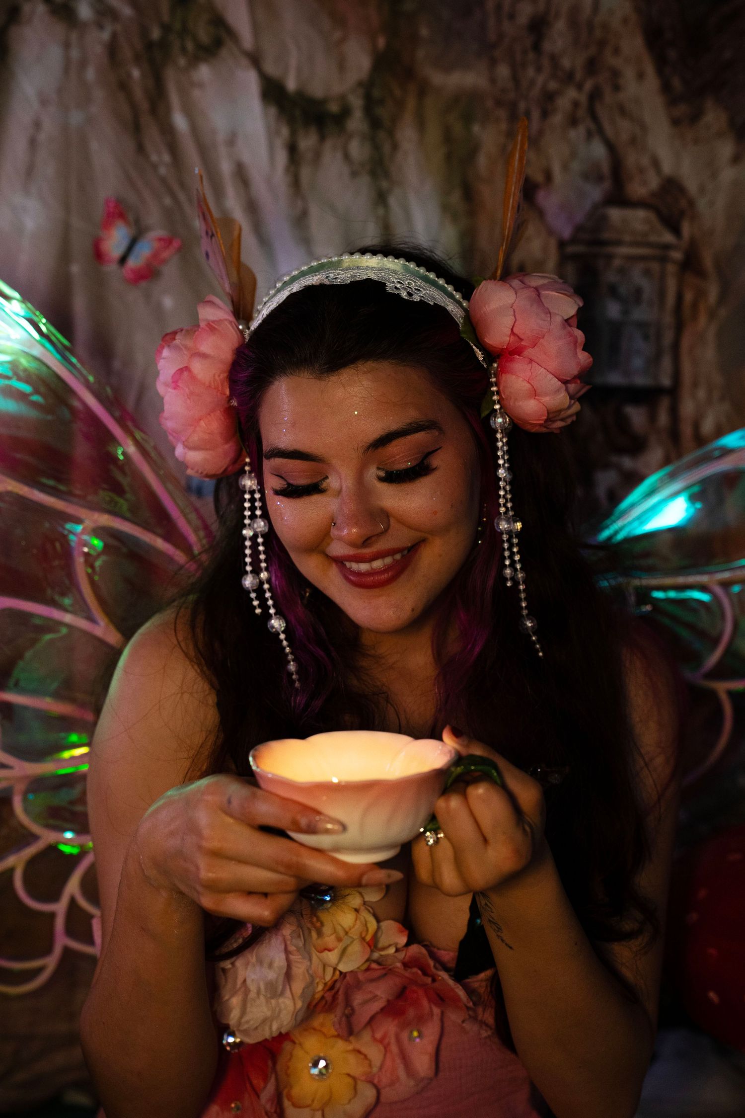 Fairy-dressed woman smiles warmly while holding illuminated lotus flower candle in magical dark forest setting. Fantasy Photoshoot