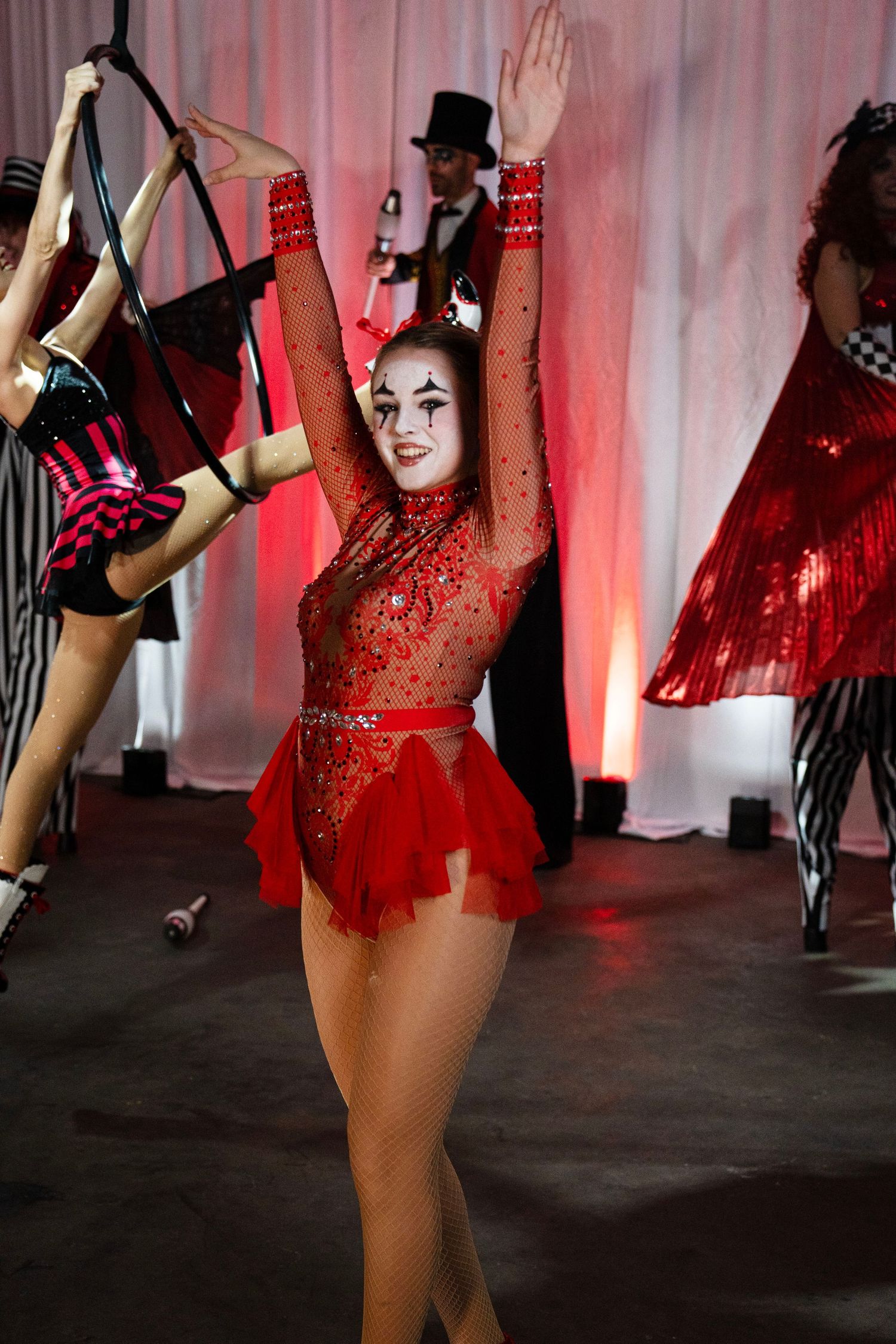 A female circus performer in a red rhinestone bodysuit with clown makeup dances at a circus show.