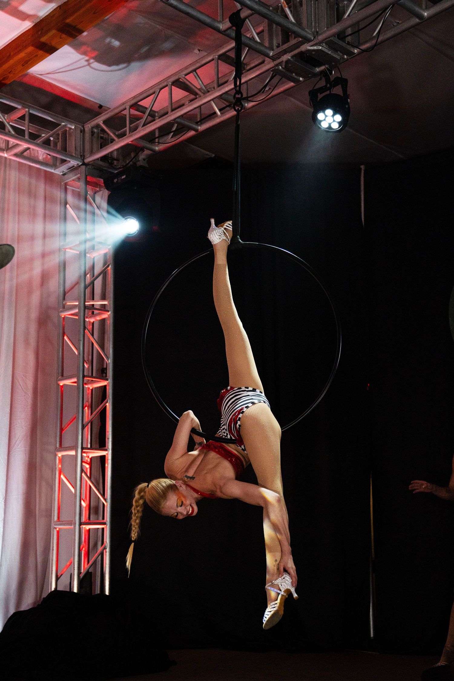 Female aerialist performs inverted split on aerial hoop in patriotic costume under stage lighting. Circus Photoshoot