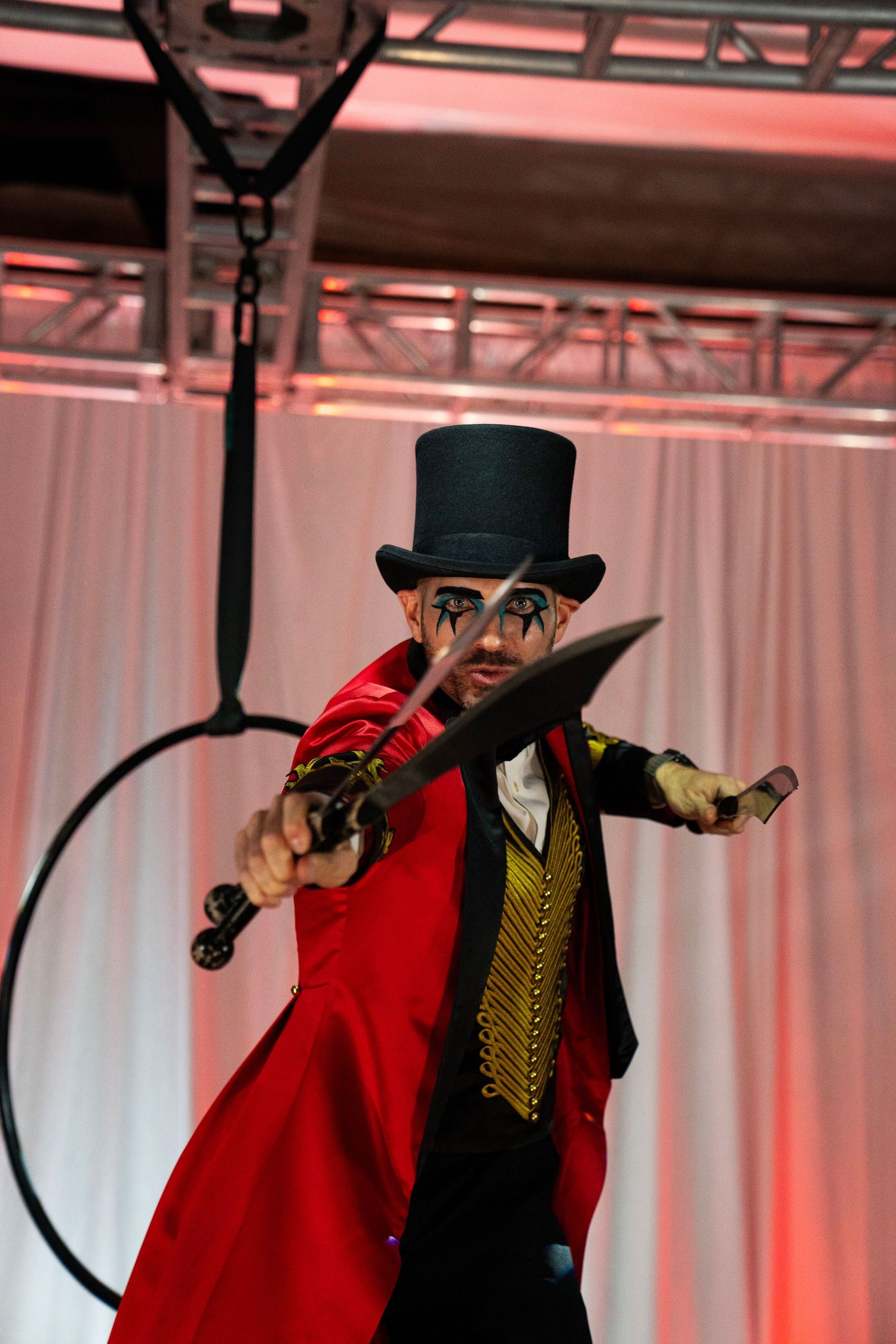 Circus ringmaster in red coat and top hat dramatically points a knife toward the camera on stage.