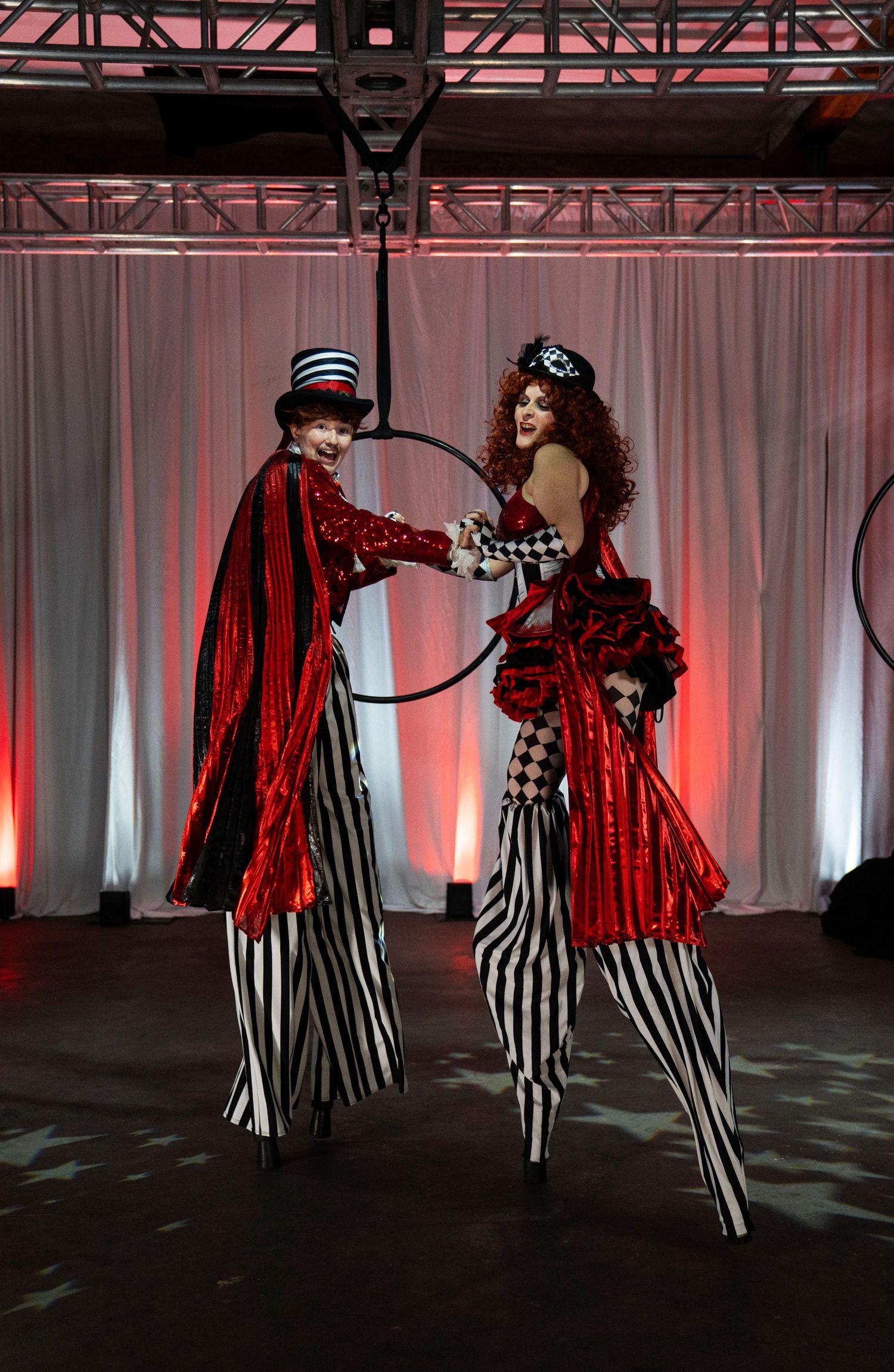 Two circus stilt walkers in red and black striped costumes pose together at event. Circus Photoshoot