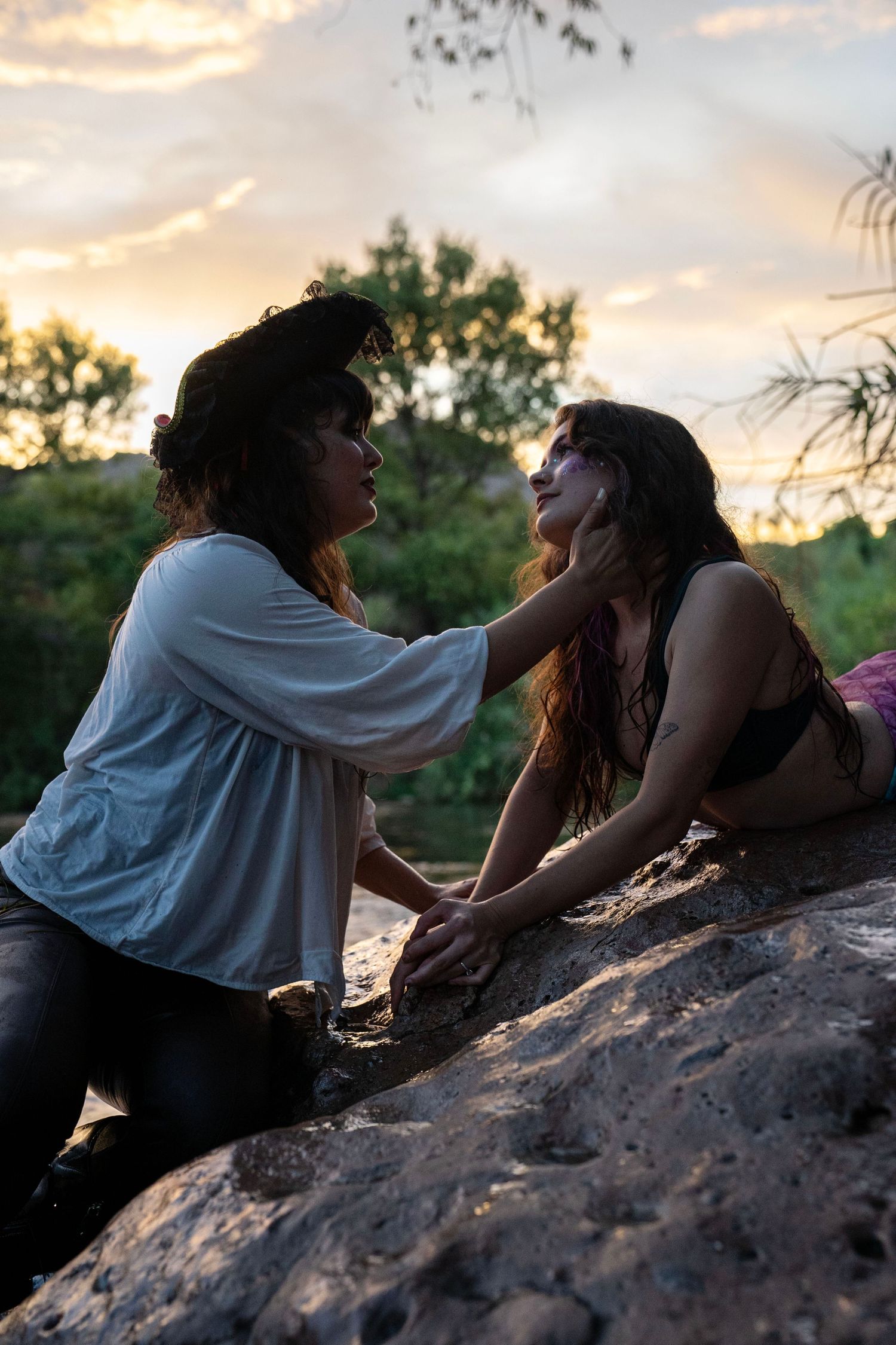 Two women in fantasy costumes holding hands on rocks near a river at sunset. Mermaid photoshoot, fantasy photoshoot. Arizona photographer.